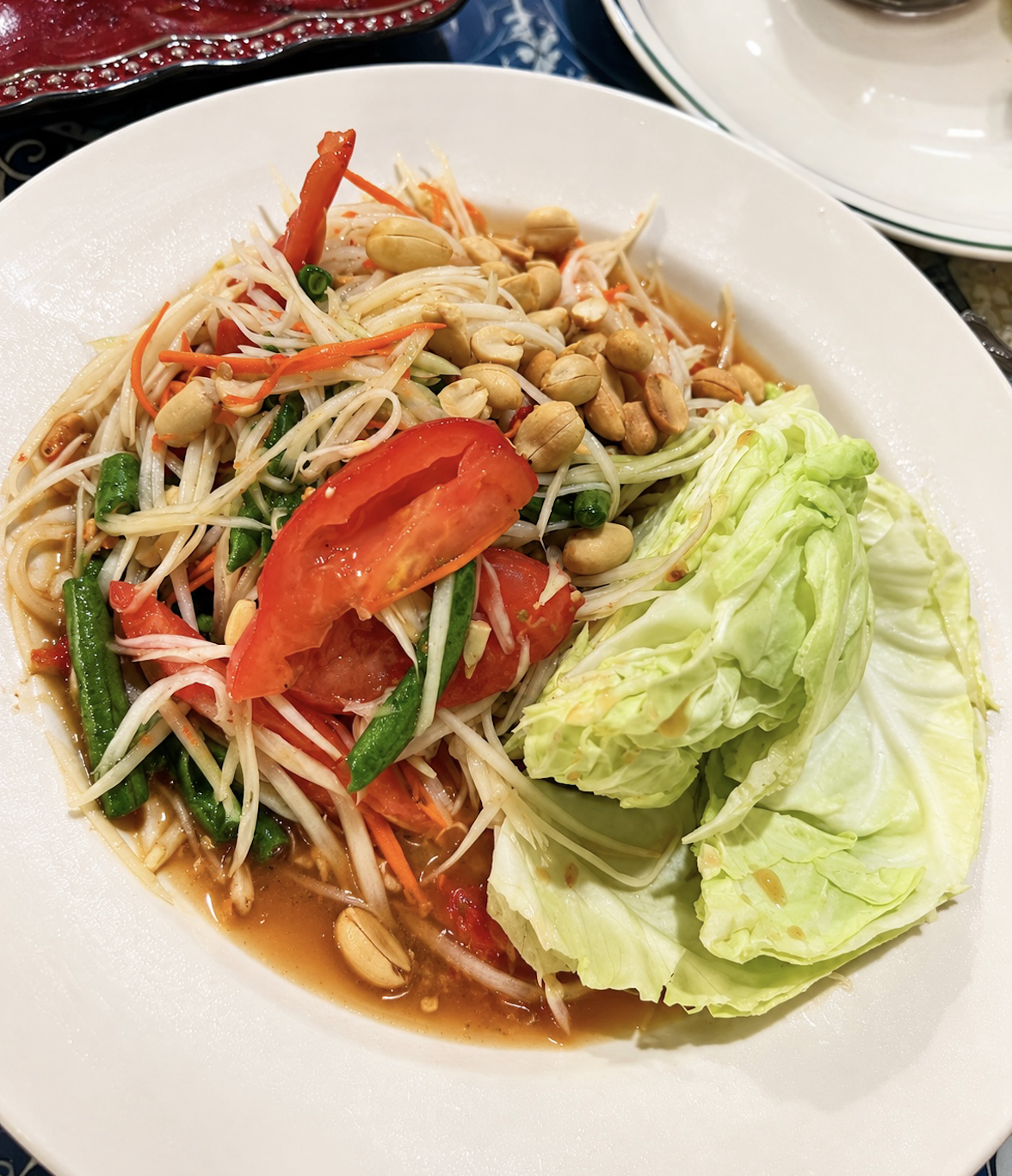 A plate of Thai green papaya salad with shredded green papaya, cherry tomatoes, peanuts, green beans, carrots, and cabbage.