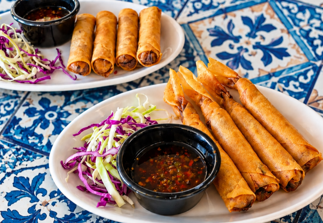 Two white plates with spring rolls, shredded cabbage salad, and dipping sauce on a blue patterned table.