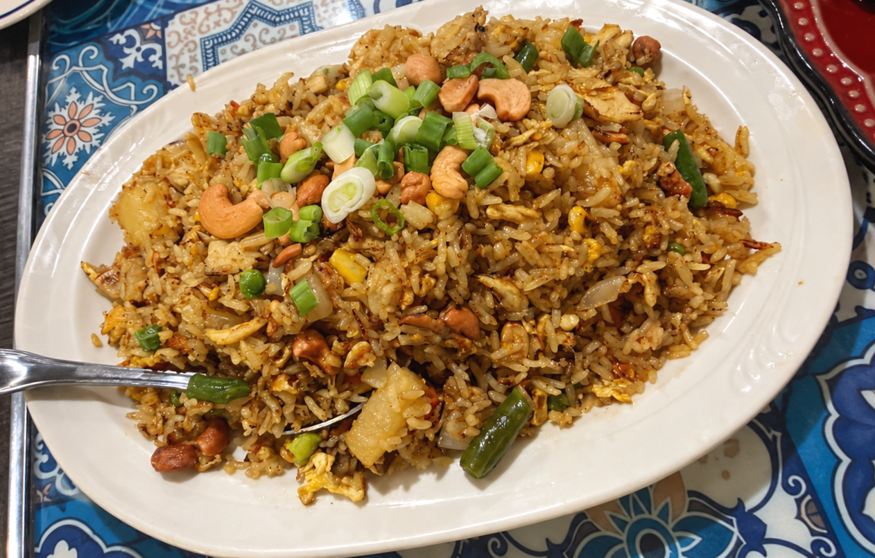 Plate of fried rice garnished with chopped green onions and cashew nuts on decorative blue and white tablecloth.