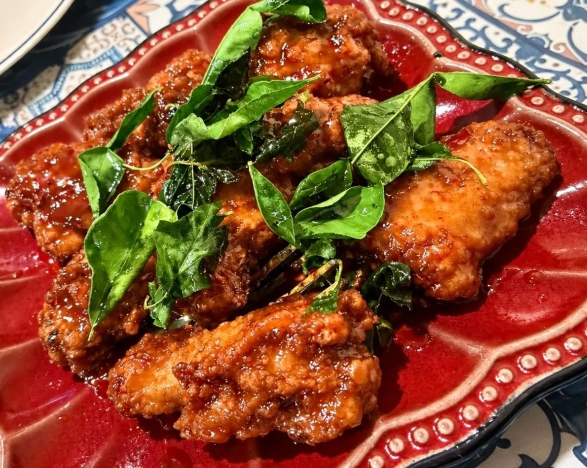Fried chicken drizzled with sauce and garnished with fresh green herbs on a decorative red plate.