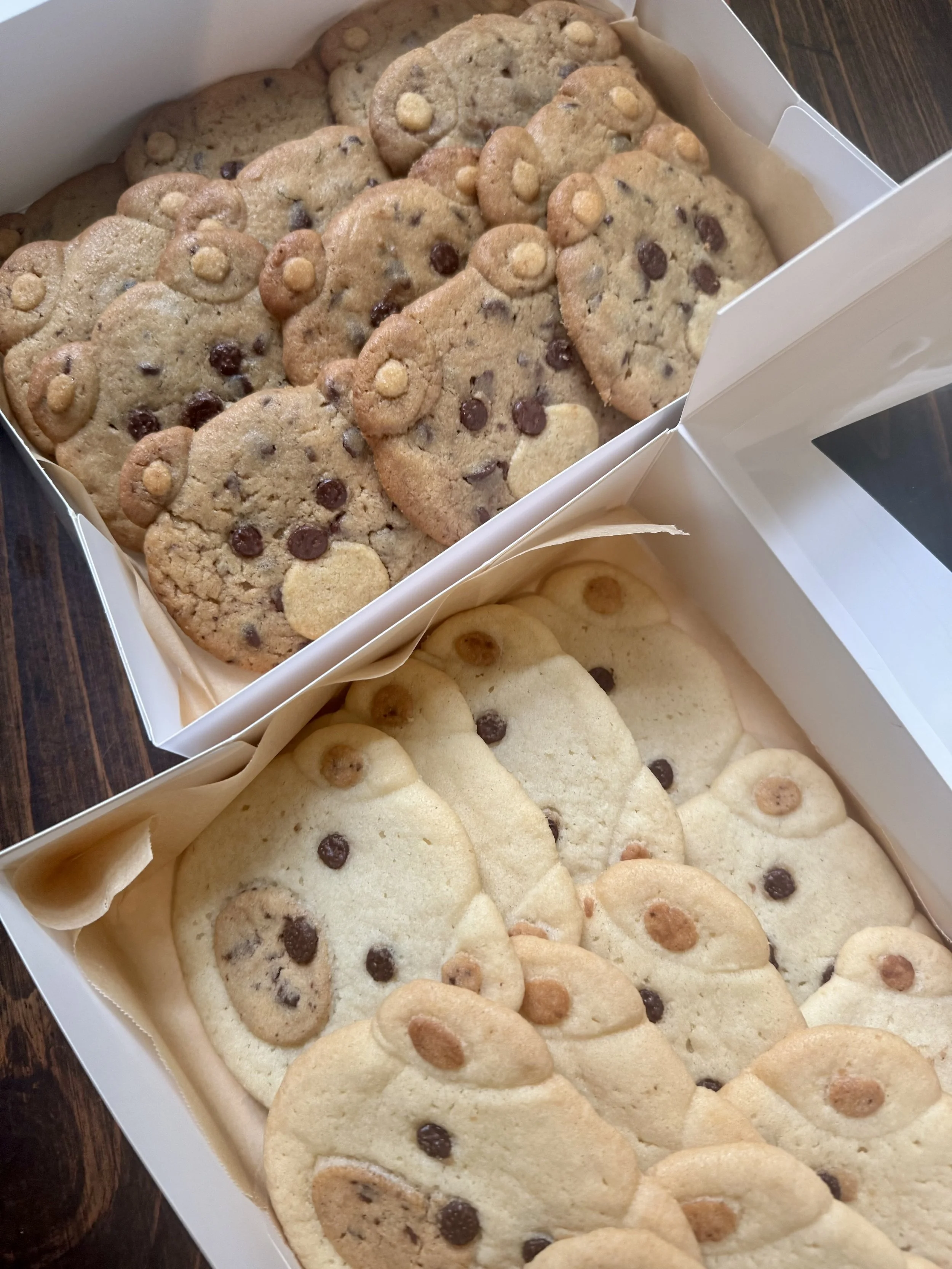 A box of assorted cookies, including chocolate chip cookies and sugar cookies with chocolate chip and peanut butter cup toppings.