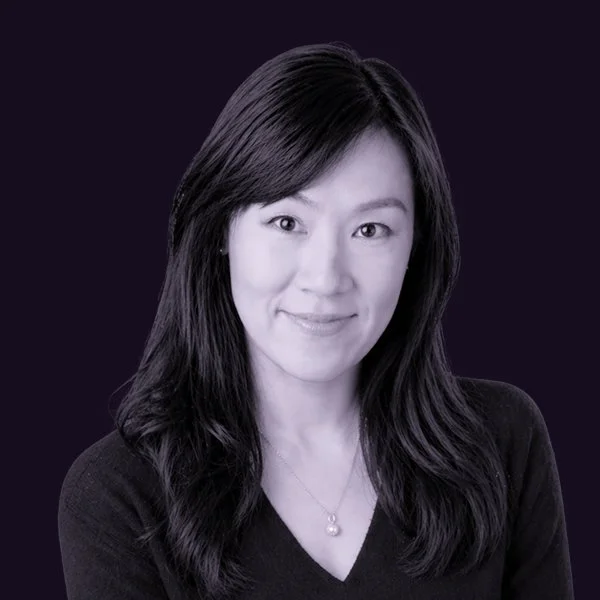 A portrait of Miranda Yang with dark hair and light skin, wearing a black top and a pearl necklace, against a dark background.