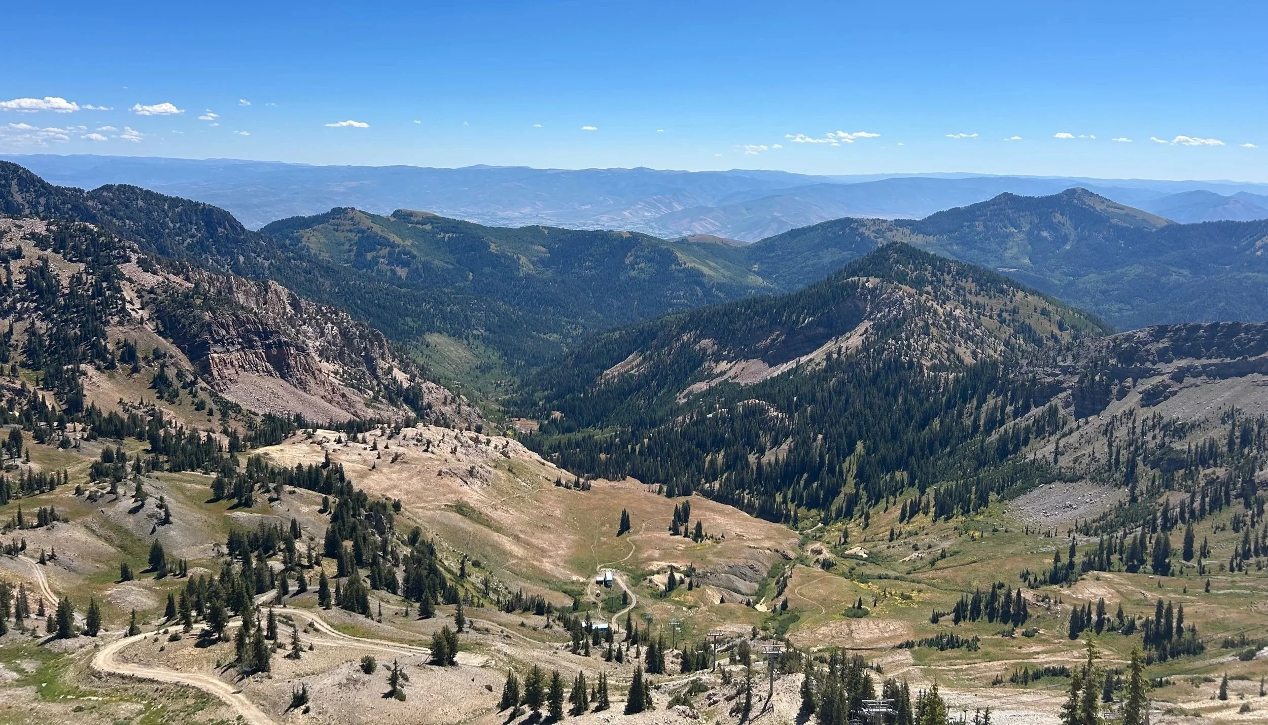 Scenic view of distant mountains, valleys, and forested hills under a clear blue sky in a mountainous landscape.