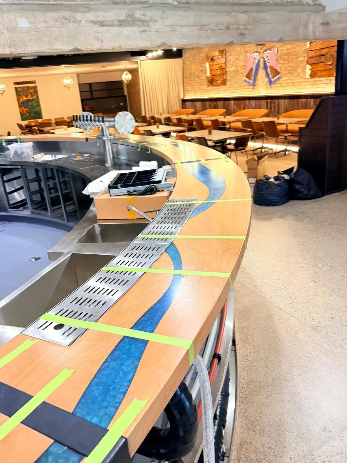 Looking along the curved bartop during installation, with the blue resin river running its full length and joints taped while the finish cures.
