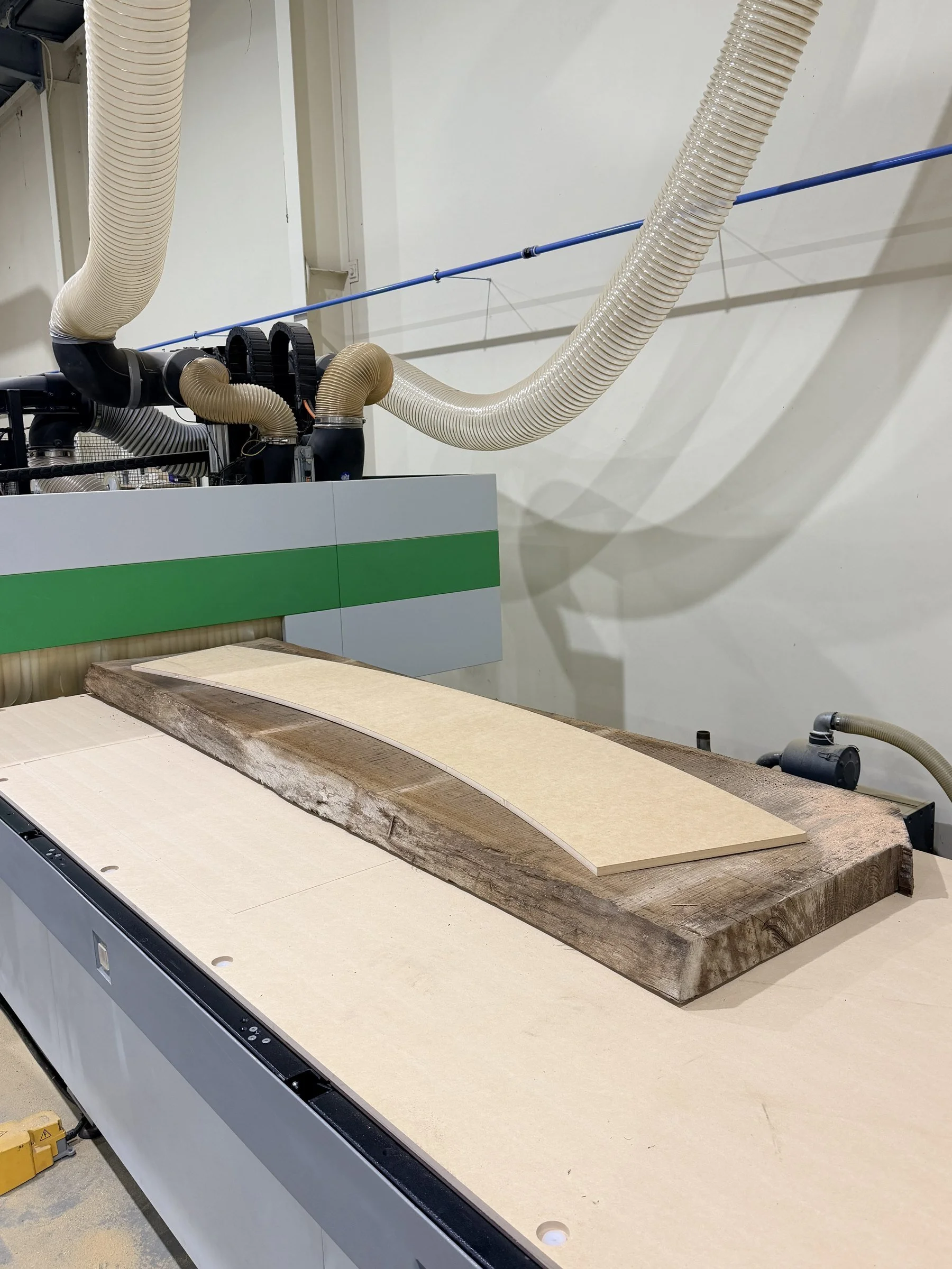 Step 2: a timber section clamped to a template on the CNC machine bed, ready to be cut to the bar's curve.
