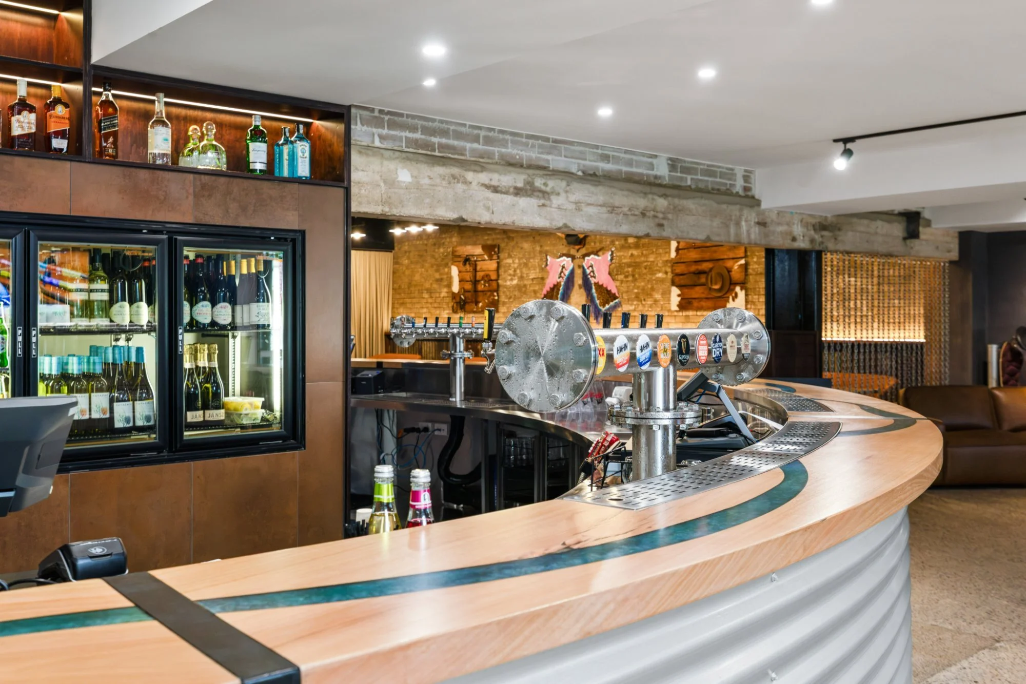 Curved timber bartop with its blue resin river sweeping past the beer taps and back bar at Bluehole Steakhouse.