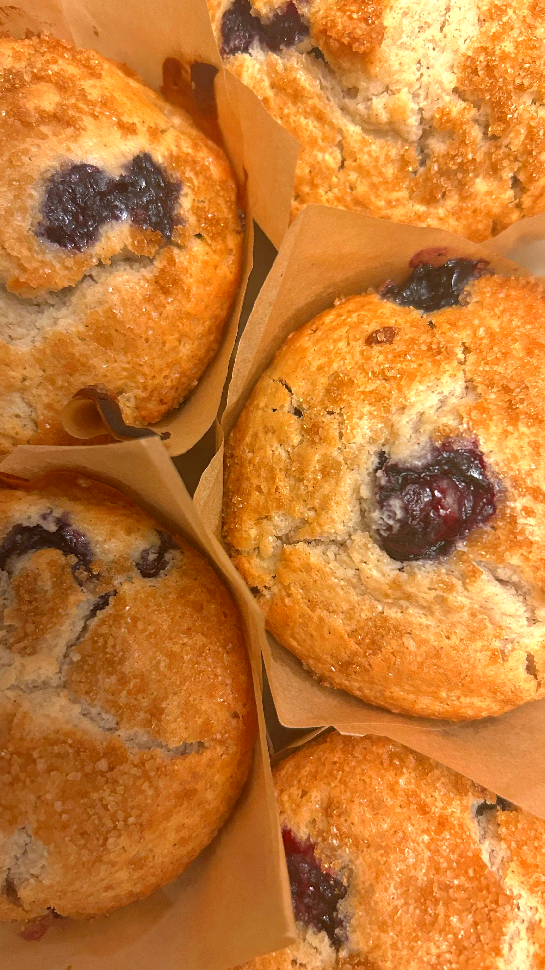 Close-up of blueberry muffins wrapped in brown paper, showing golden-brown tops with some blueberries peeking through