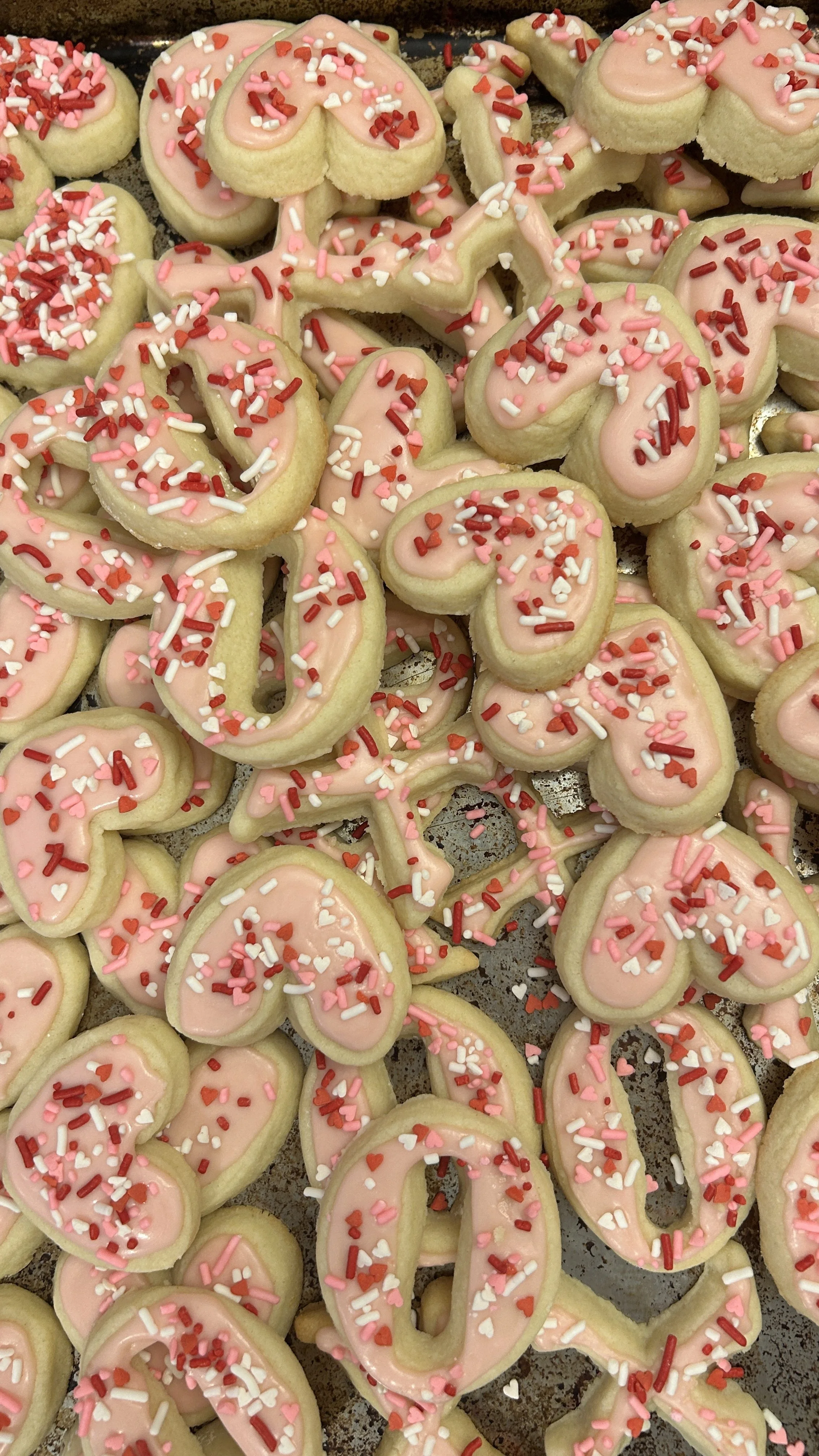 Close-up of Valentine-themed sugar cookies decorated with pink icing and red, pink, white, and heart-shaped sprinkles.