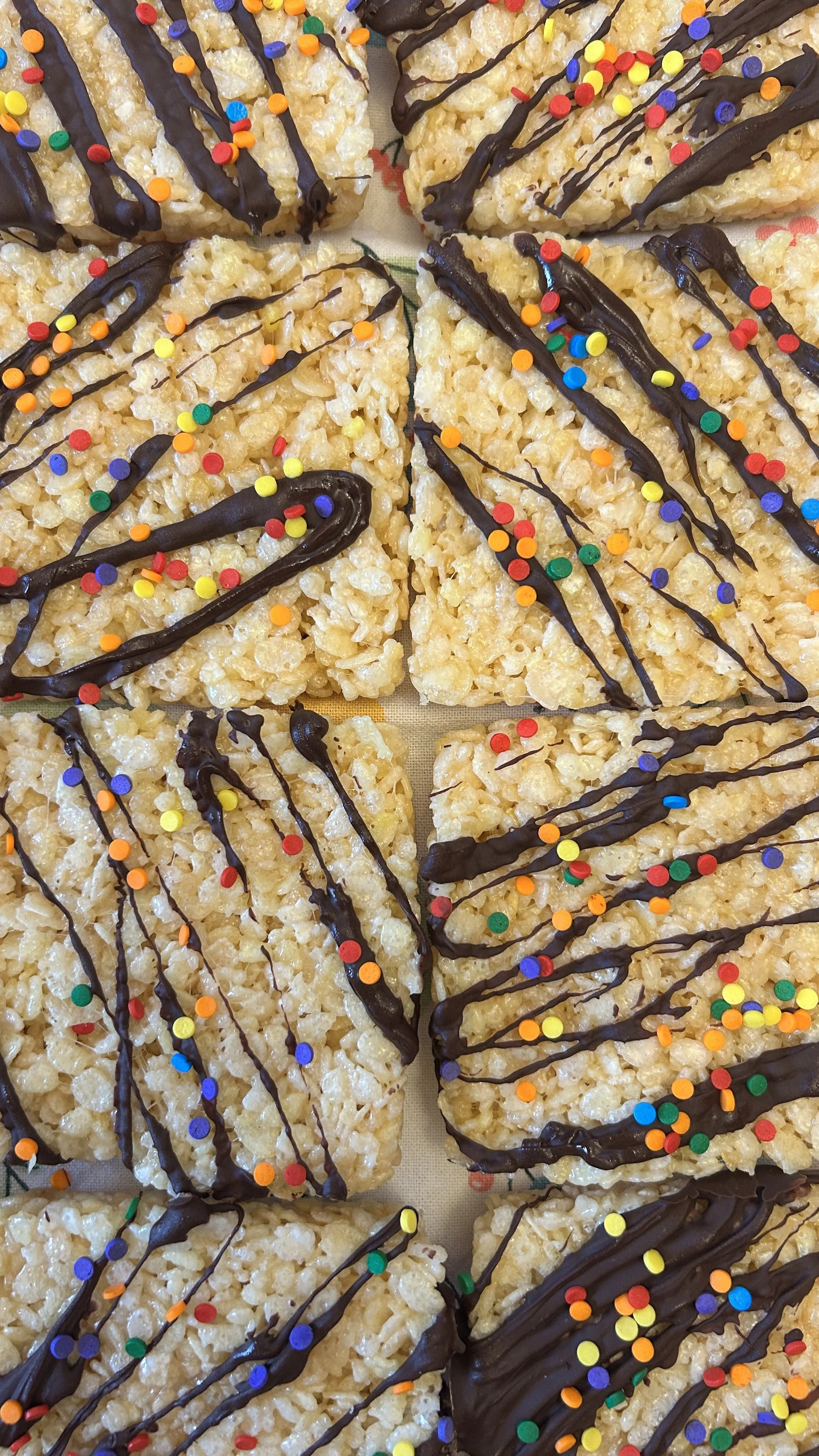 Rice krispie treats topped with colorful sprinkles and drizzled with chocolate.