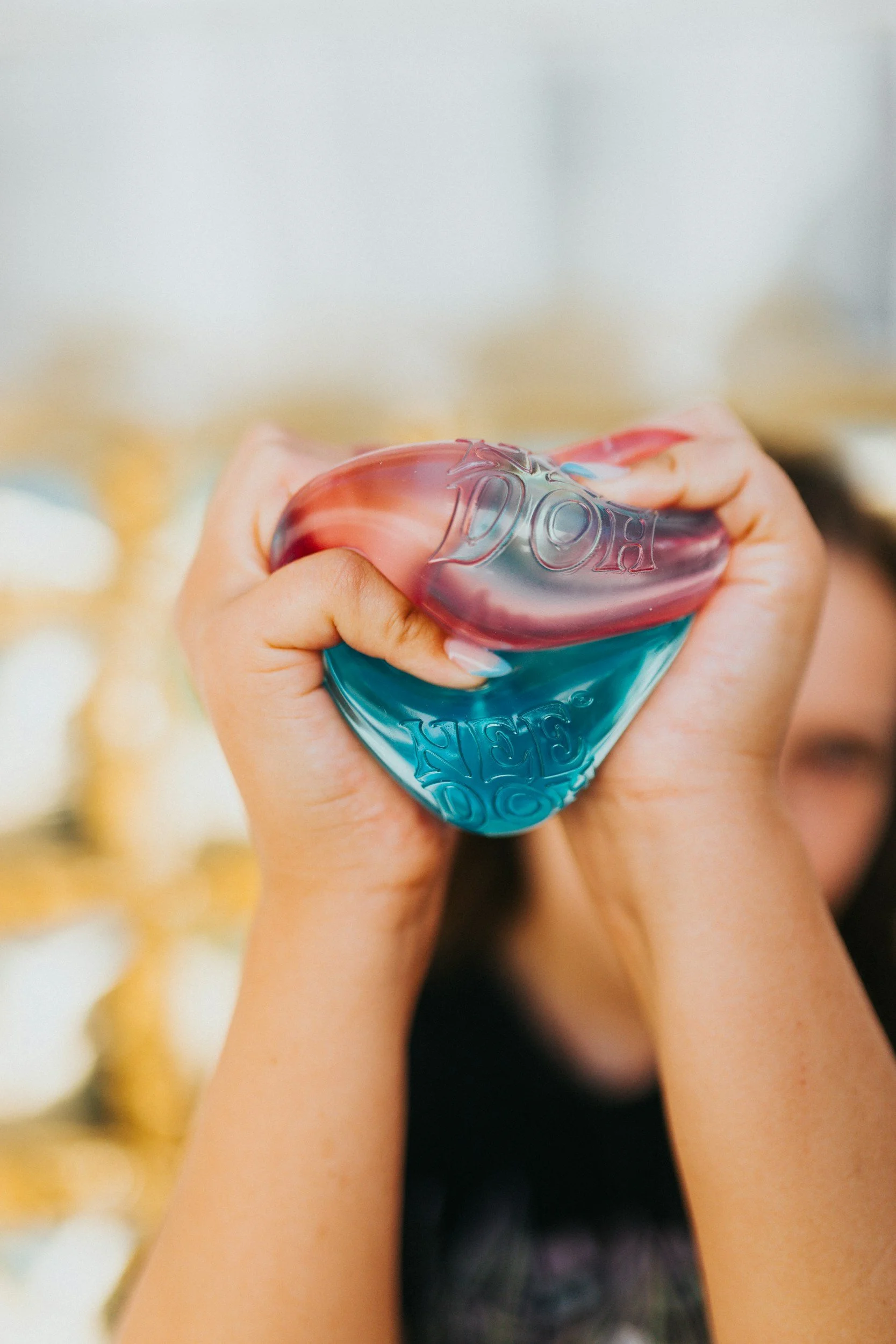 Person holding a squeezable plastic toy in the shape of a heart, with pink and blue colors and embossed text.