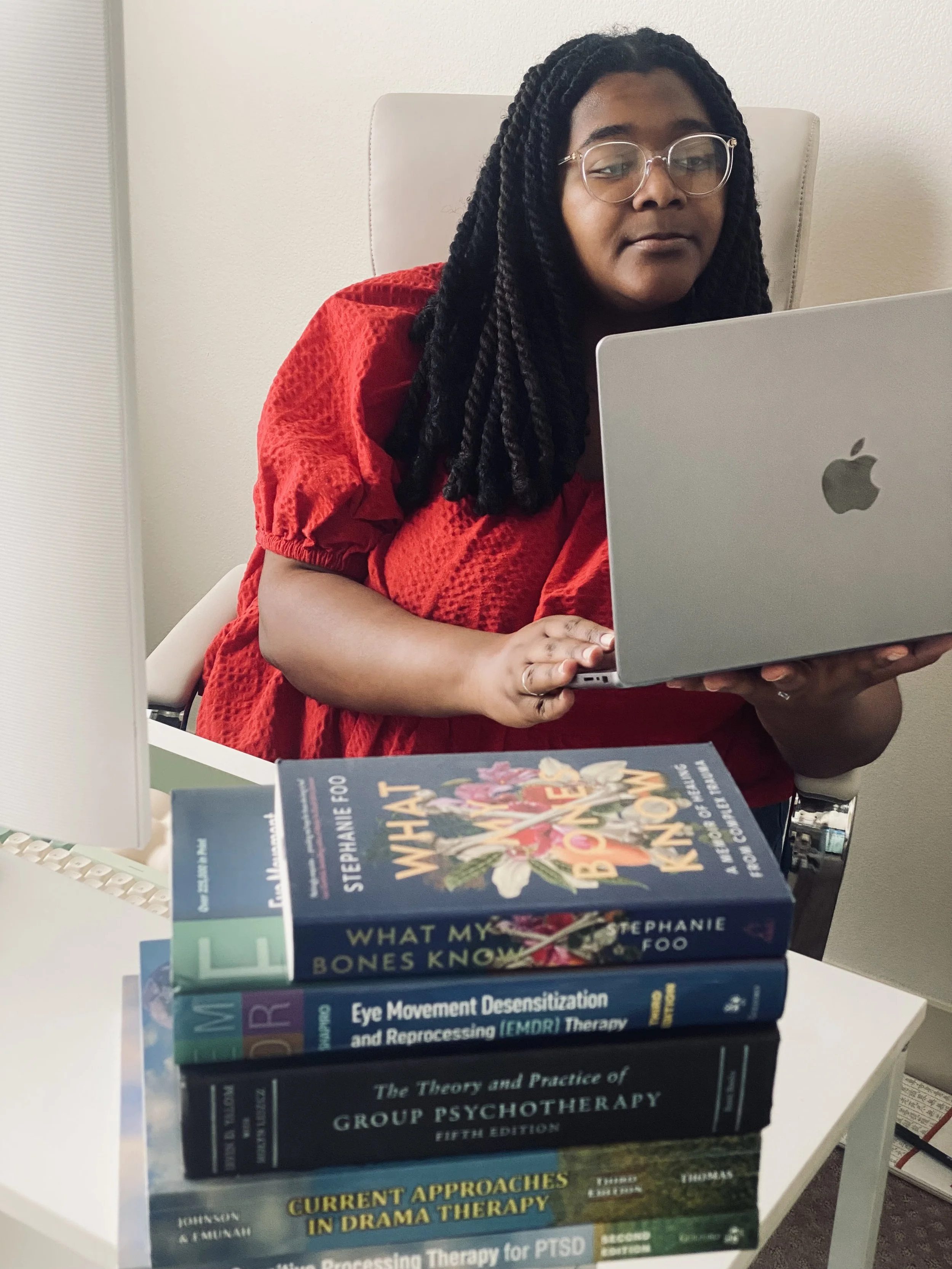 Trinity Perry seated at a desk with a laptop and therapy books.