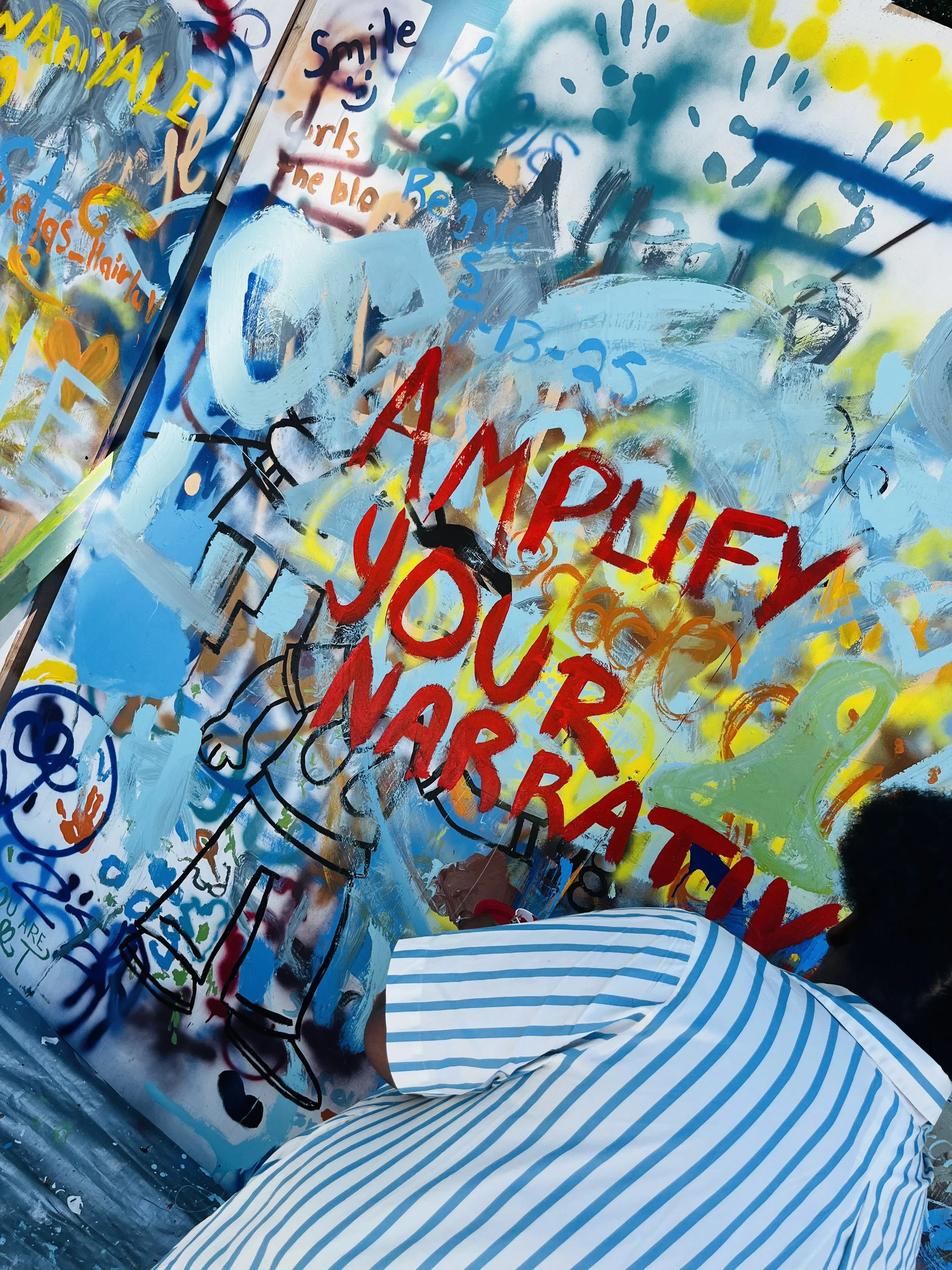 Trinity Perry creating a colorful “Amplify Your Narrative” mural.