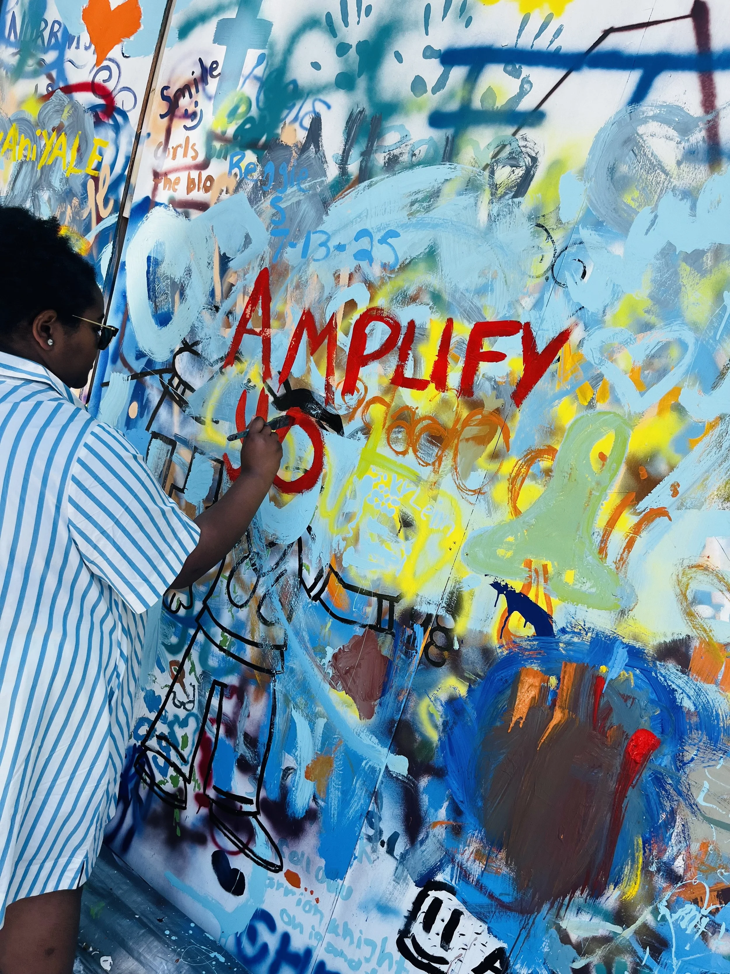 Trinity Perry creating a colorful “Amplify Your Narrative” mural.