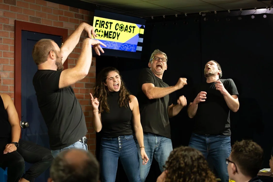 People performing a comedy show on stage at First Coast Comedy with an audience watching.