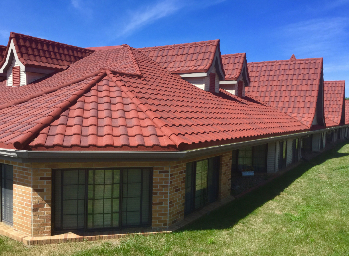 A house with a red tiled roof, brick exterior walls, and large windows, under a clear blue sky.