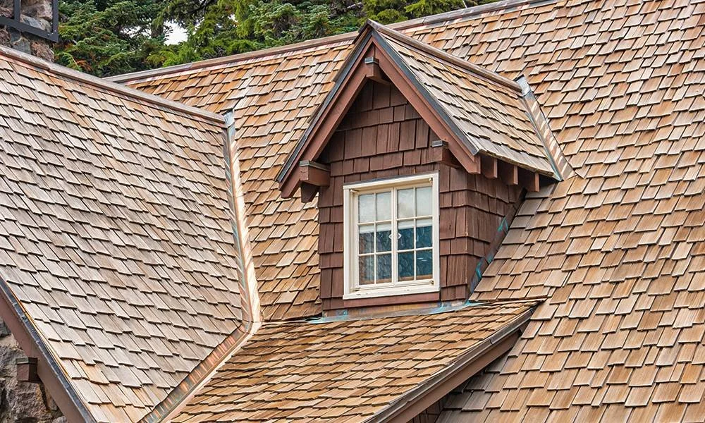 Close-up of a house roof with a dormer window and wooden shingles.