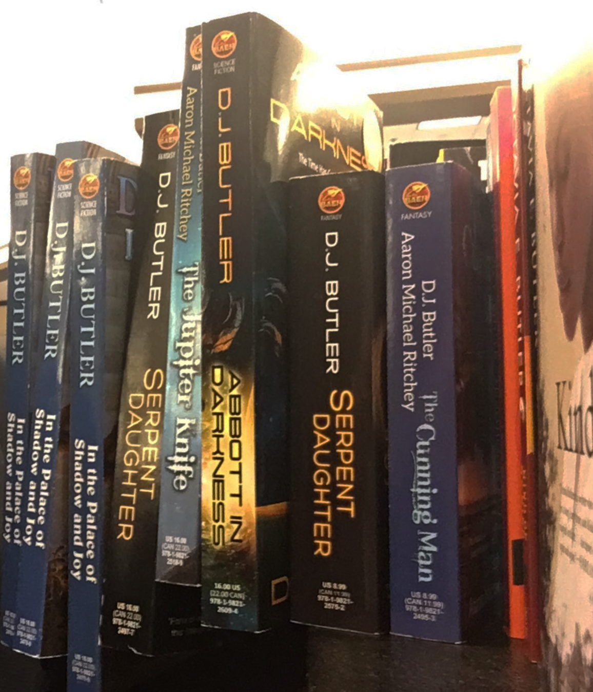 Shelf of science fiction books by D.J. Butler, including 'Serpent in the Star' and 'The Trumpeting Man'.