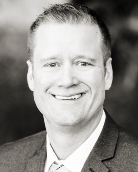 Black and white portrait of a smiling man with short hair, wearing a suit and tie.