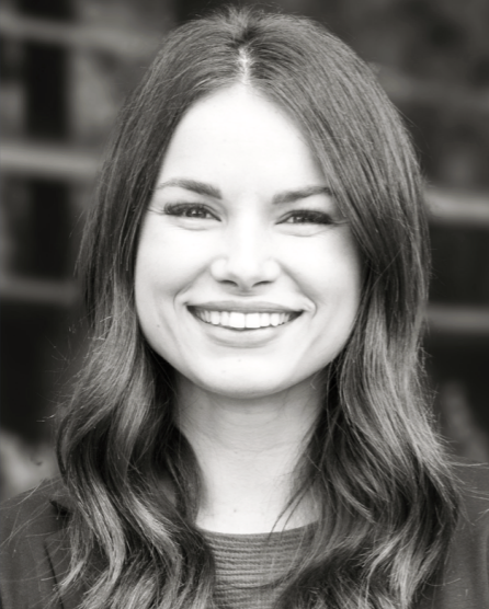 A young woman with long wavy hair smiling in an outdoor setting.