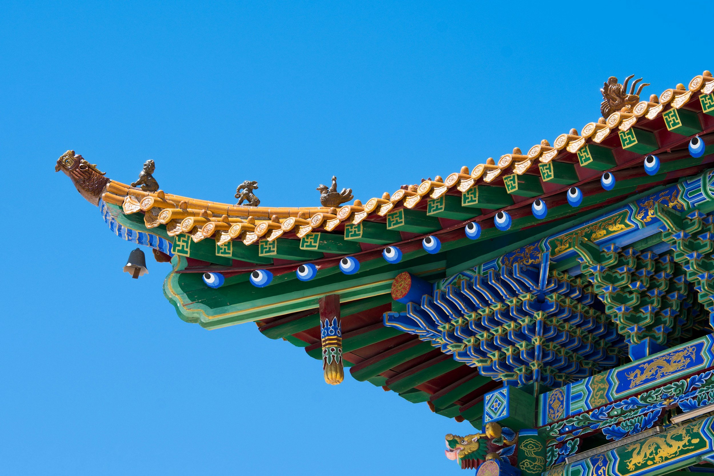 Close-up photo of a colorful traditional Asian temple roof with intricate designs and decorative elements, set against a bright blue sky.