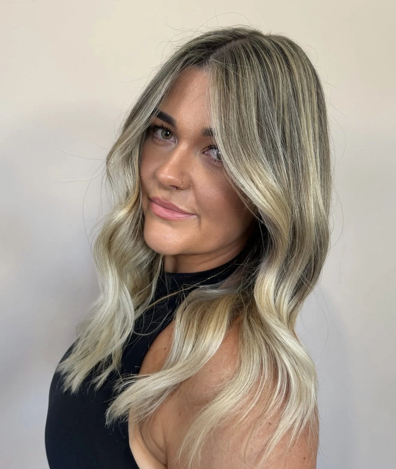Close-up of a woman with blonde, wavy hair and green eyes, wearing a black top, against a plain white background.