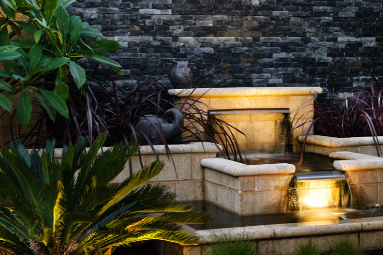 A decorative outdoor water fountain illuminated with Hunza pond lights us and LuxR New Zealand designed and made outdoor garden lights