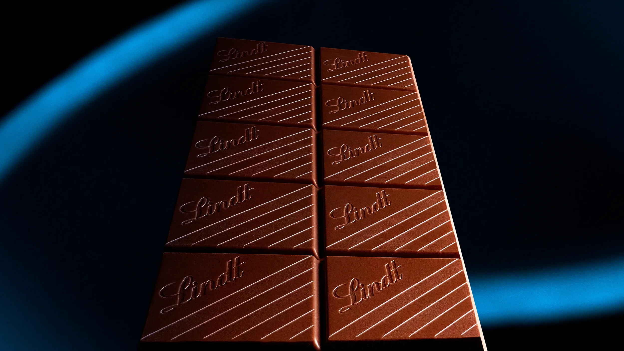 Tablette de chocolat au lait Lindt avec une surface lisse et des lignes en relief sur un fond noir.