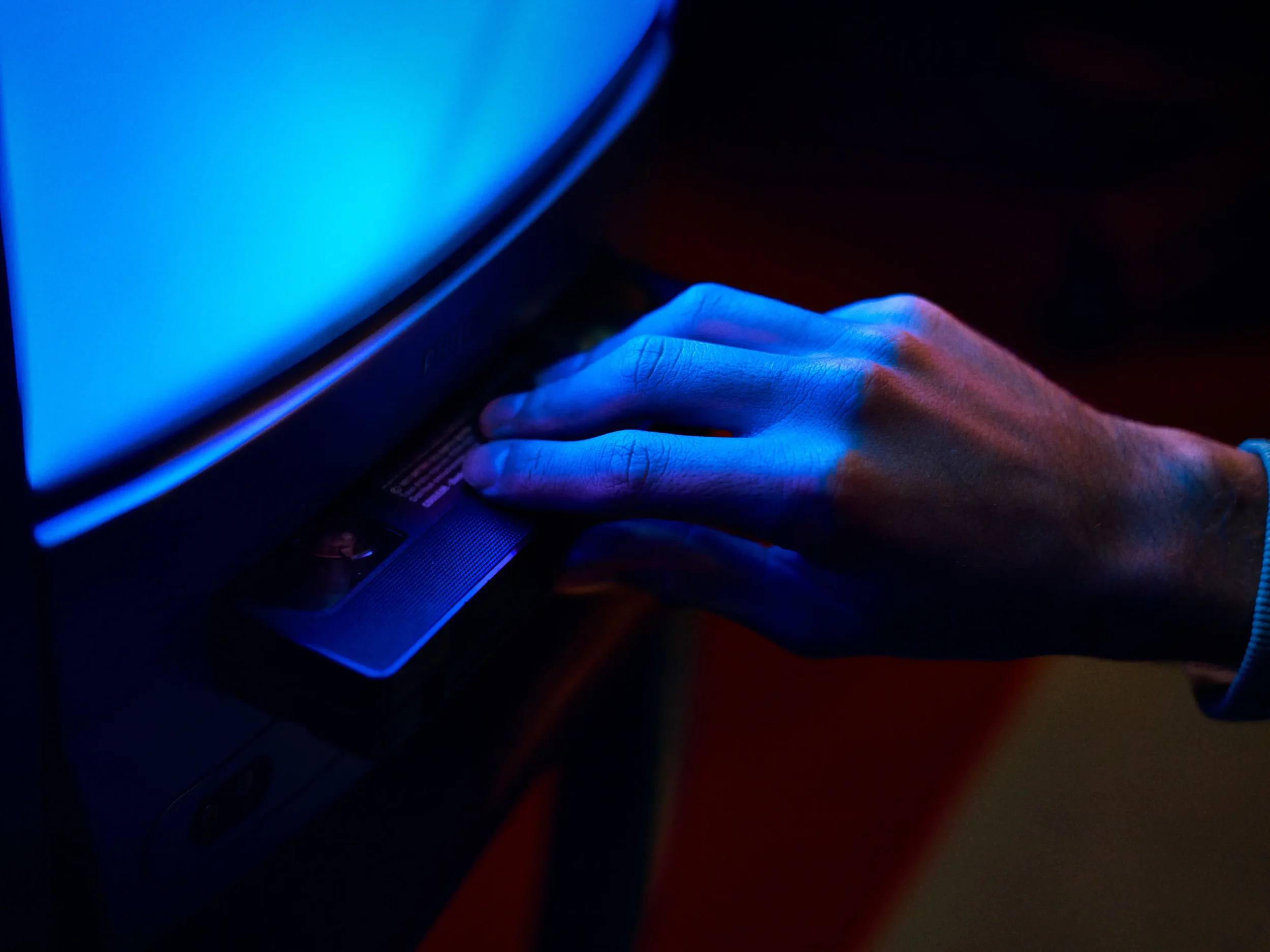 Une main touche un ordinateur portable dont l'écran est éclairé en bleu, dans l'obscurité.