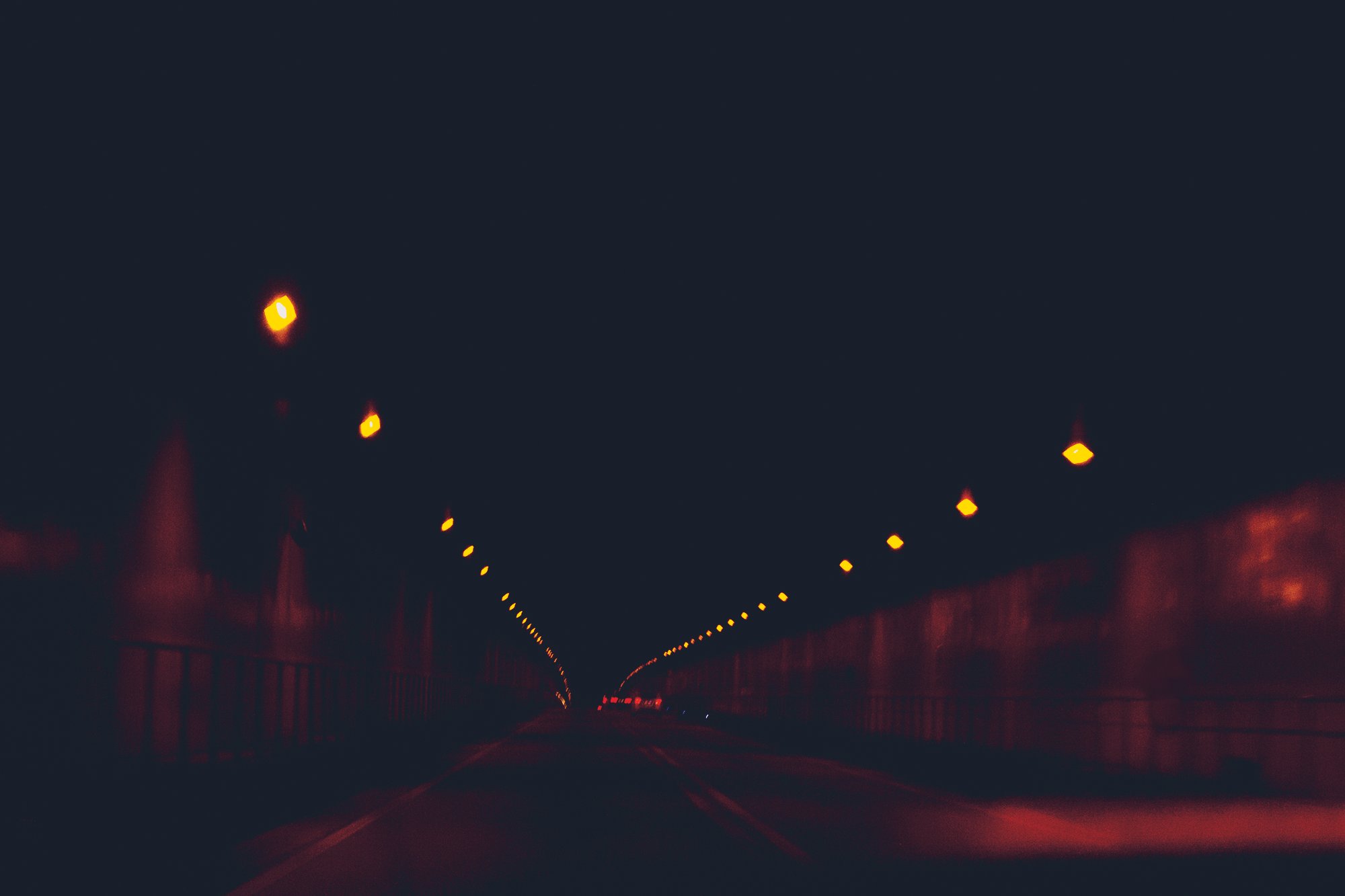 Vue nocturne d'un tunnel avec des lumières orange alignées au plafond, rideau métallique et route vide.