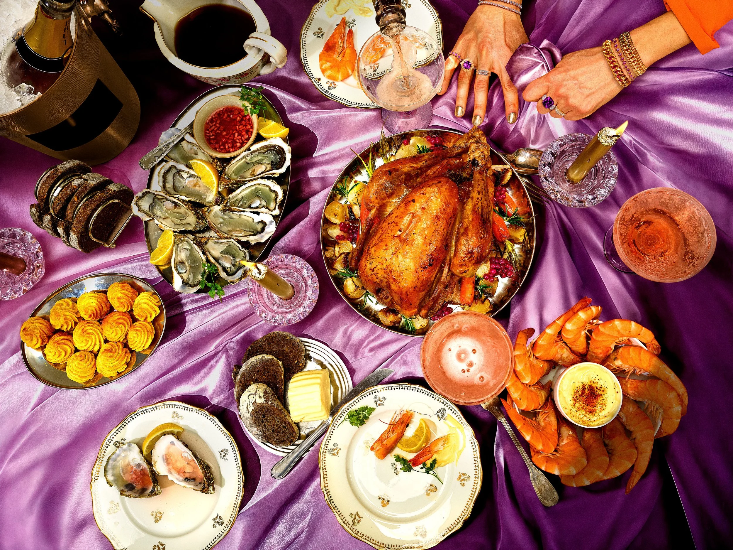 Un festin coloré comprenant des huîtres, un poulet rôti, des crevettes, des tartes, des sauces, et des biscuits, tous servis sur une nappe violette.