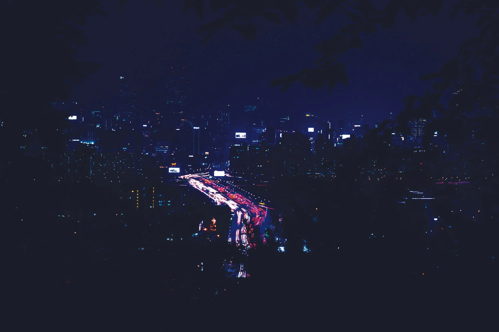 Une ville illuminée de nuit, avec des gratte-ciel et des lumières de circulation rouge et blanche sur une route principale.