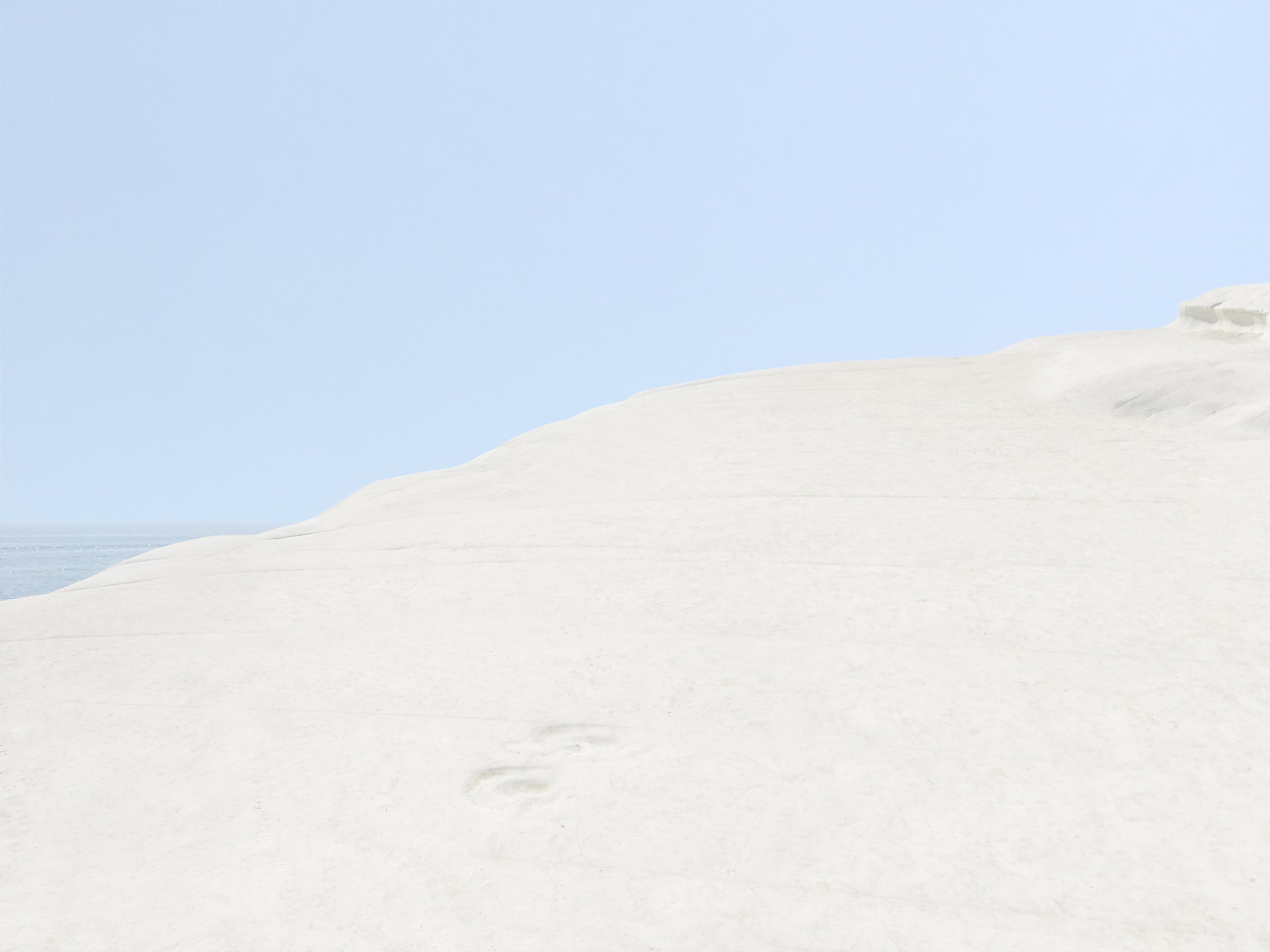Plage de sable blanc avec dunes, ciel bleu clair, et ceinture de nuages.