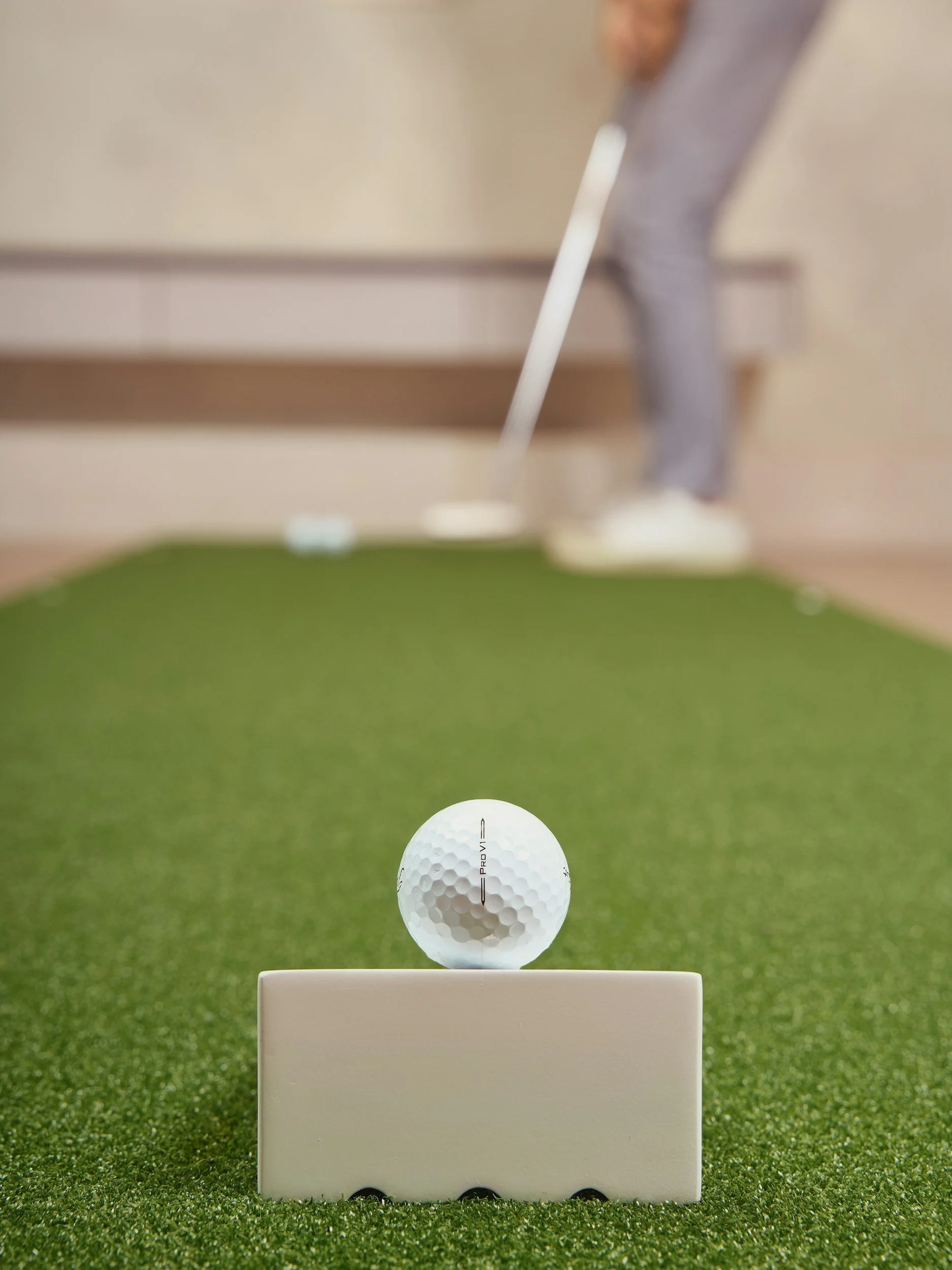 A golf ball on a tee on a green putting surface, with a golf club in the background.