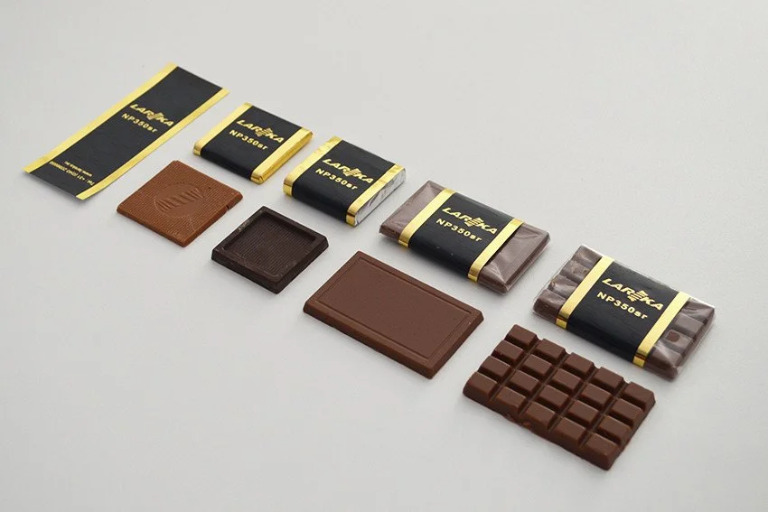 Various types of chocolate bars in different sizes with a Lareka label arranged on a light surface.