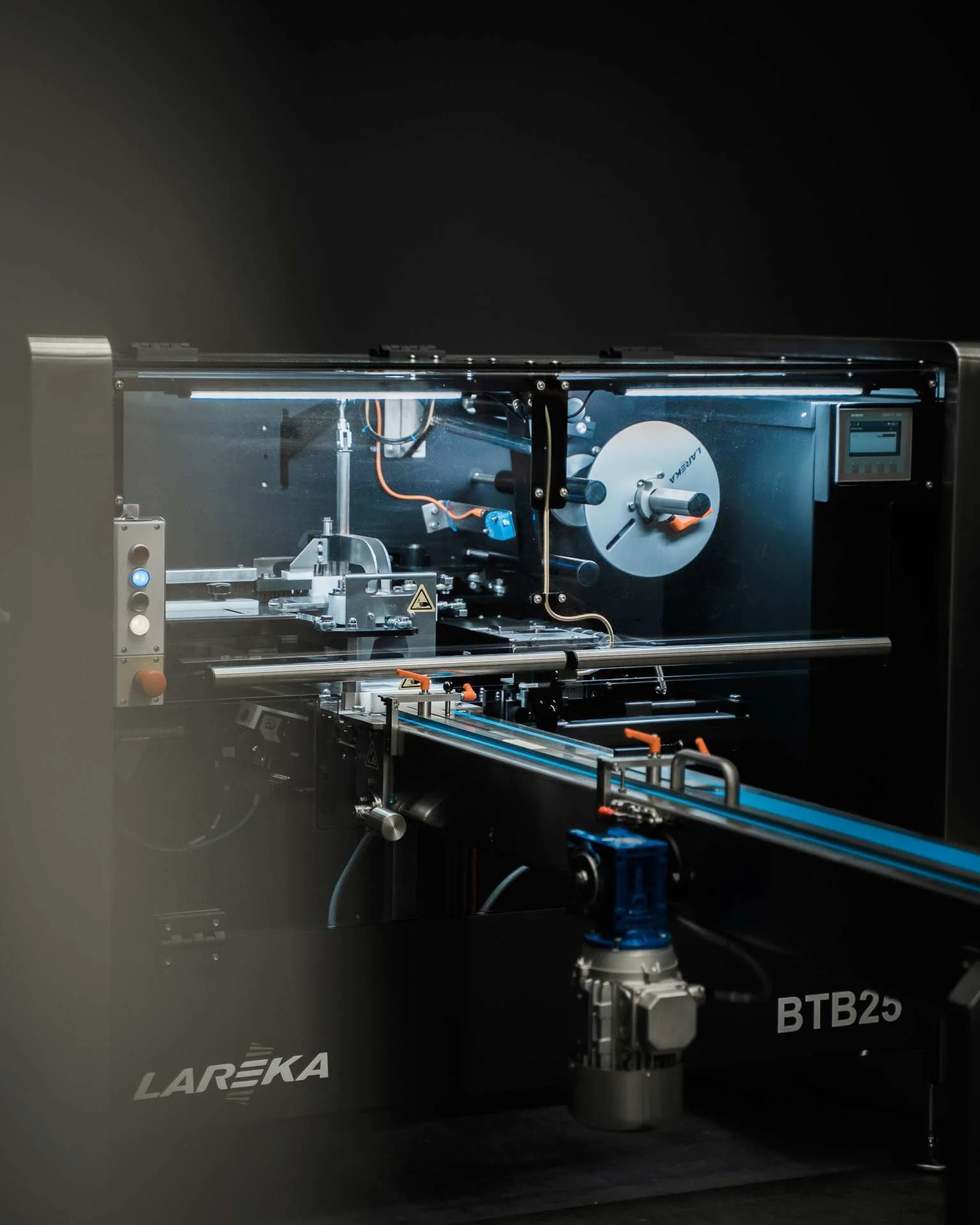 The BTB25 Lareka Chocolate Packaging Machine with a digital display, metal components, wires, and a circular disc inside a dark, enclosed environment.
