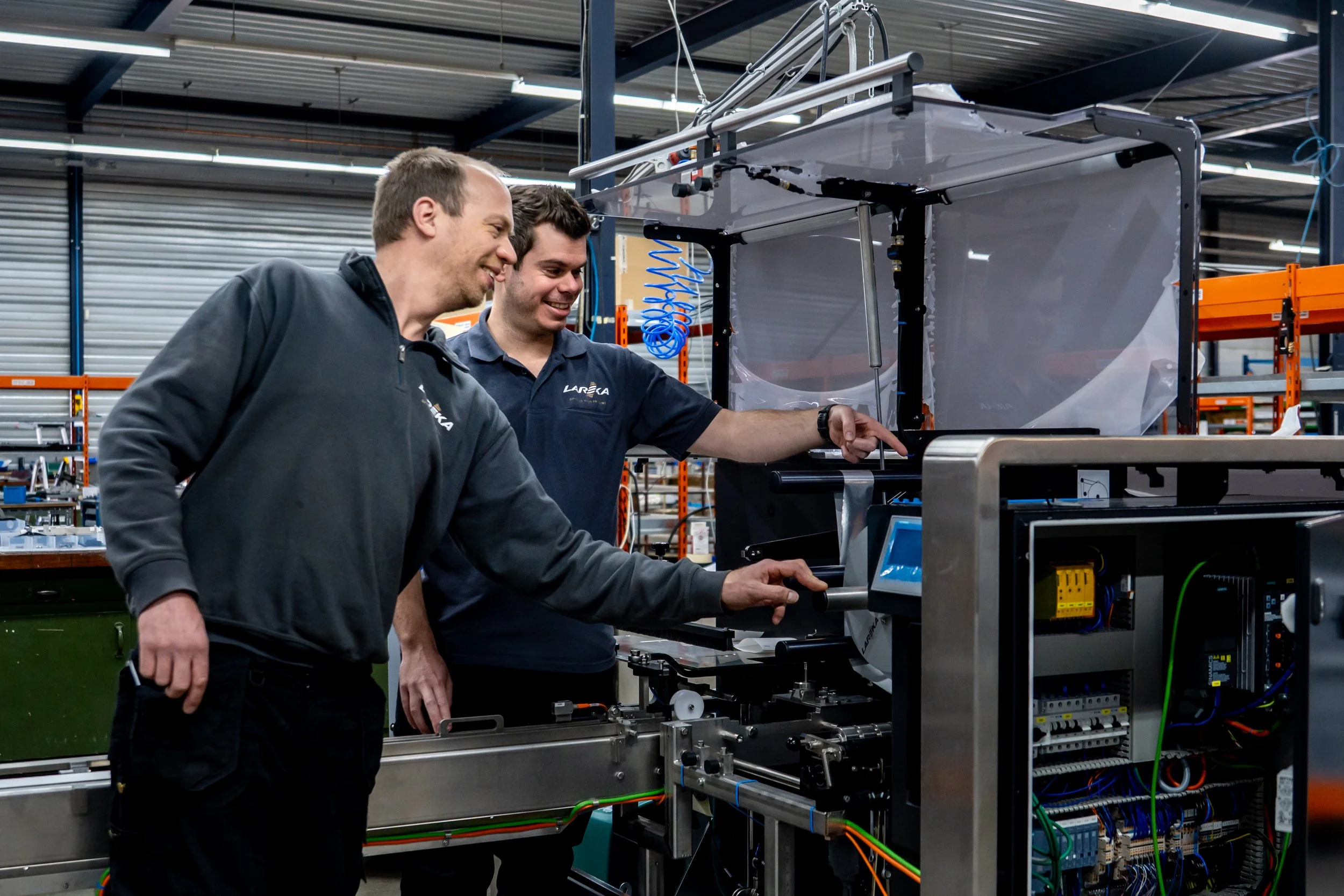 Two Lareka mechanics looking inside the Lareka BTB25 chocolate packaging machine inside an industrial factory.