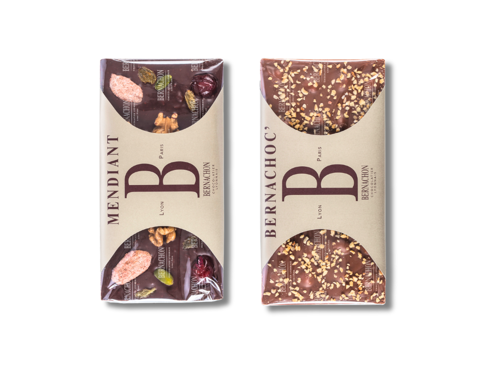 Two chocolate bars wrapped in a transparent foil and band wrap packaging style with partially open packaging revealing assorted toppings like nuts and dried fruit, branded as Bernachon, laid side by side on a white background.