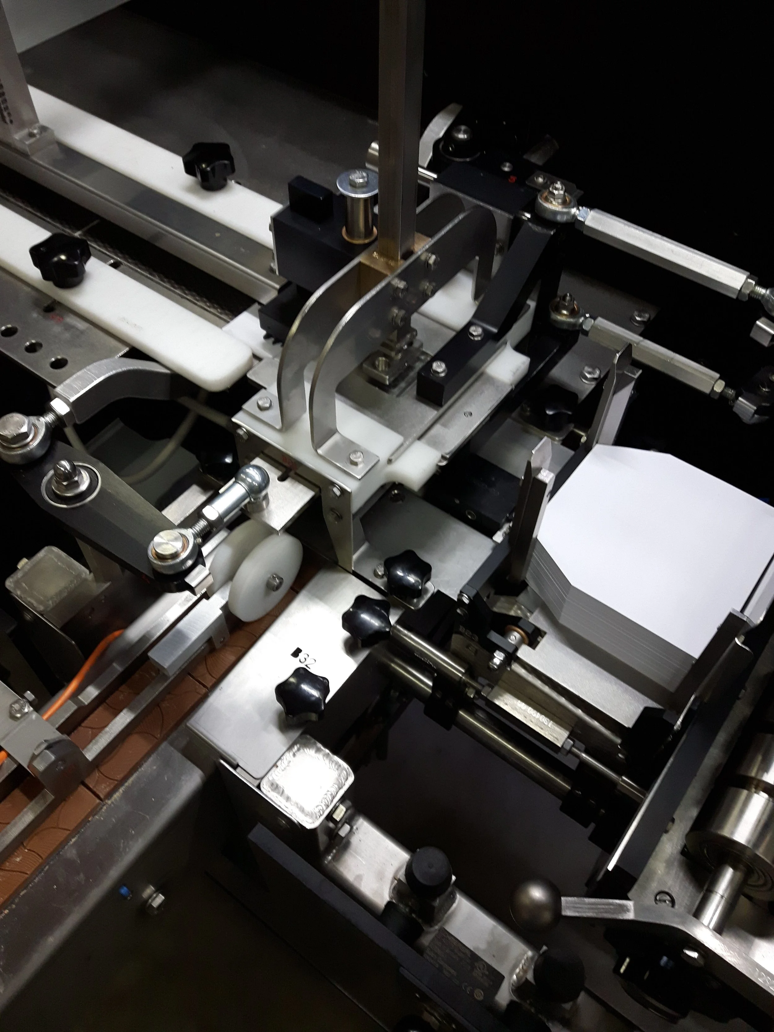 Close-up of a precision BTB25 Chocolate packaging machine with metal components, rollers, screws, and adjustment knobs.