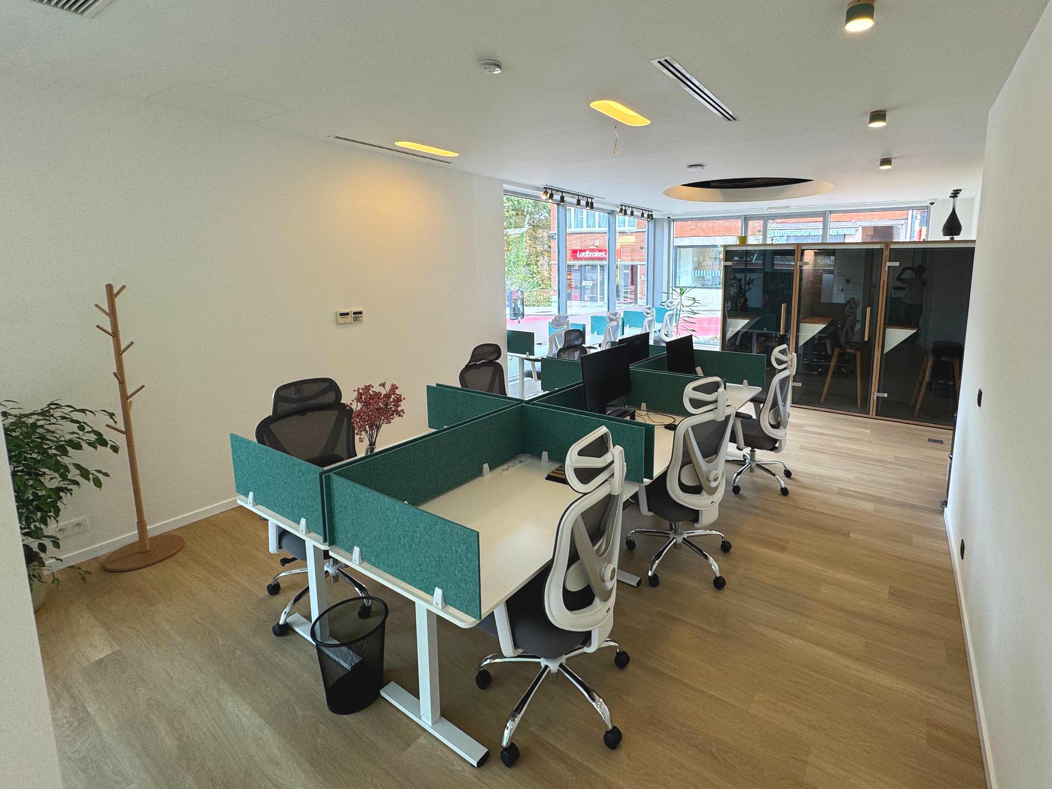 Modern office coworking space with multiple workstations, both fix and flex desks, ergonomic chairs, large windows and natural light, three phone booths