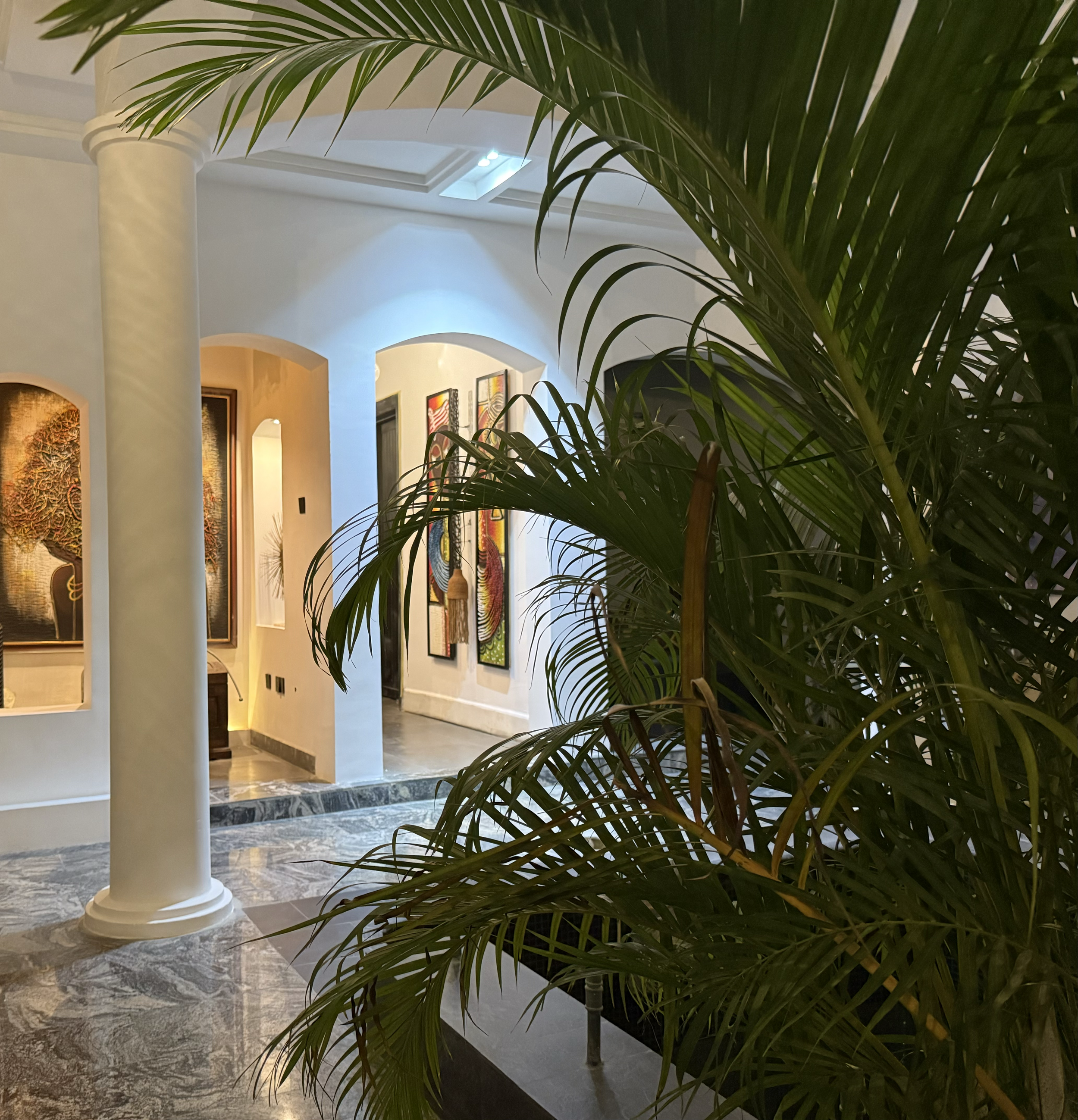 Indoor courtyard with arched walkways, framed wall-art, tall palm trees and grey marble flooring