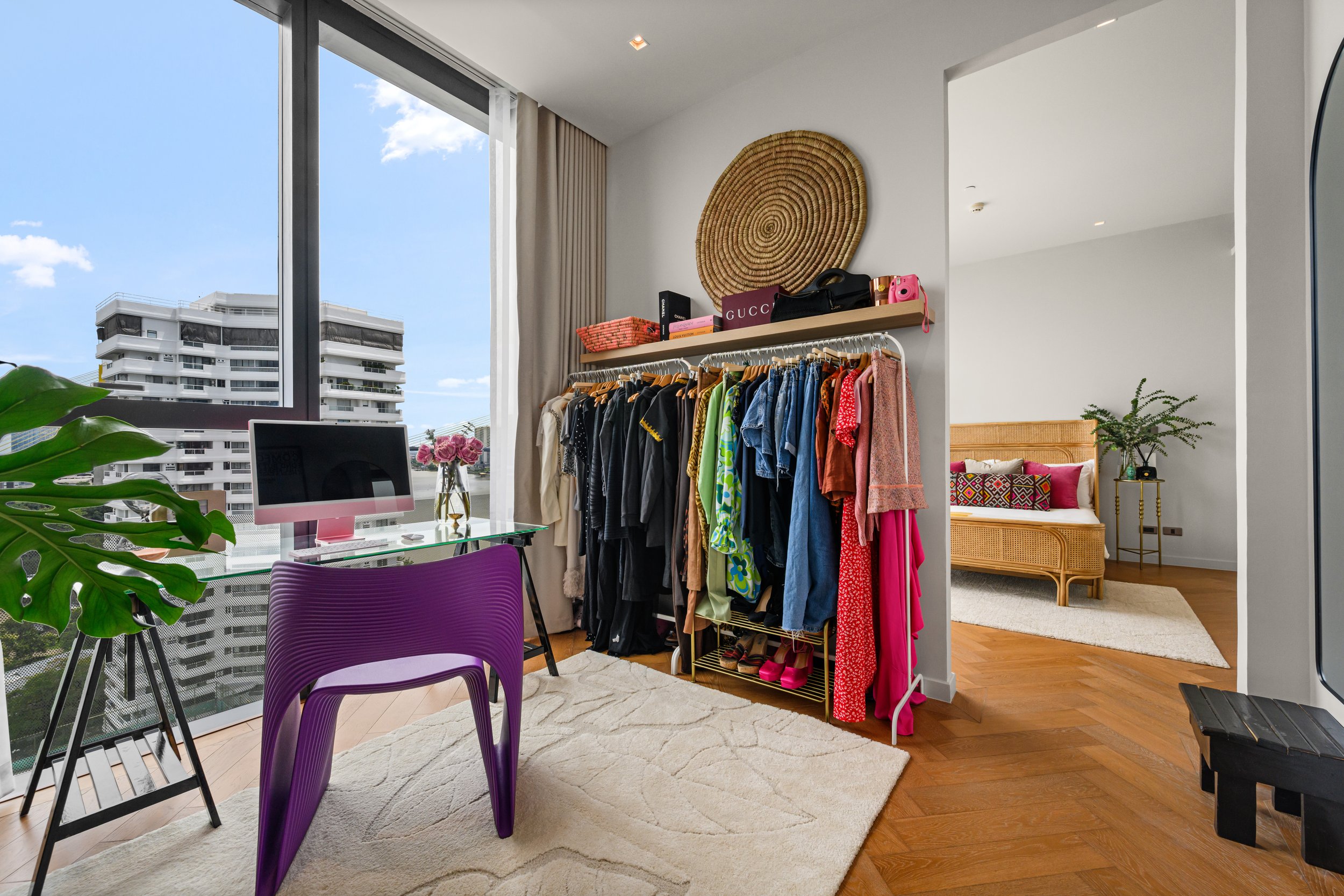 Dressing room with a sculptural purple chair, a clothes rail of colourful outfits and a round woven wall display