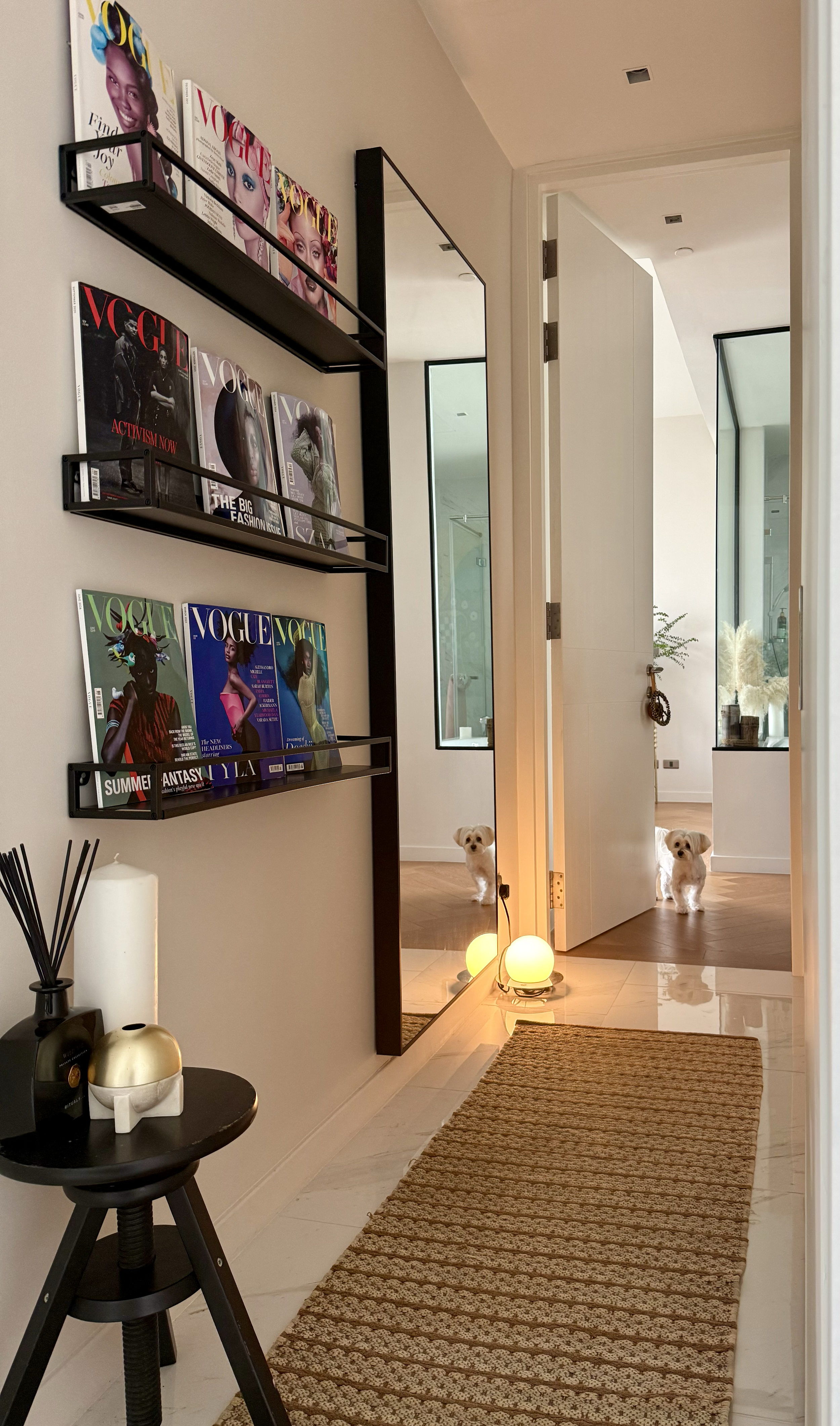 Hallway wall of British Vogue magazine covers featuring Black women, displayed on black metal shelves beside a tall mirror
