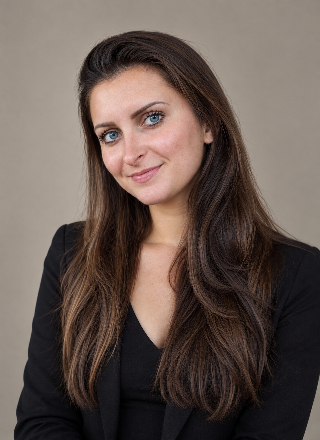 Portrait d'une femme avec des cheveux bruns, portant une veste noire, souriant légèrement, fond neutre.