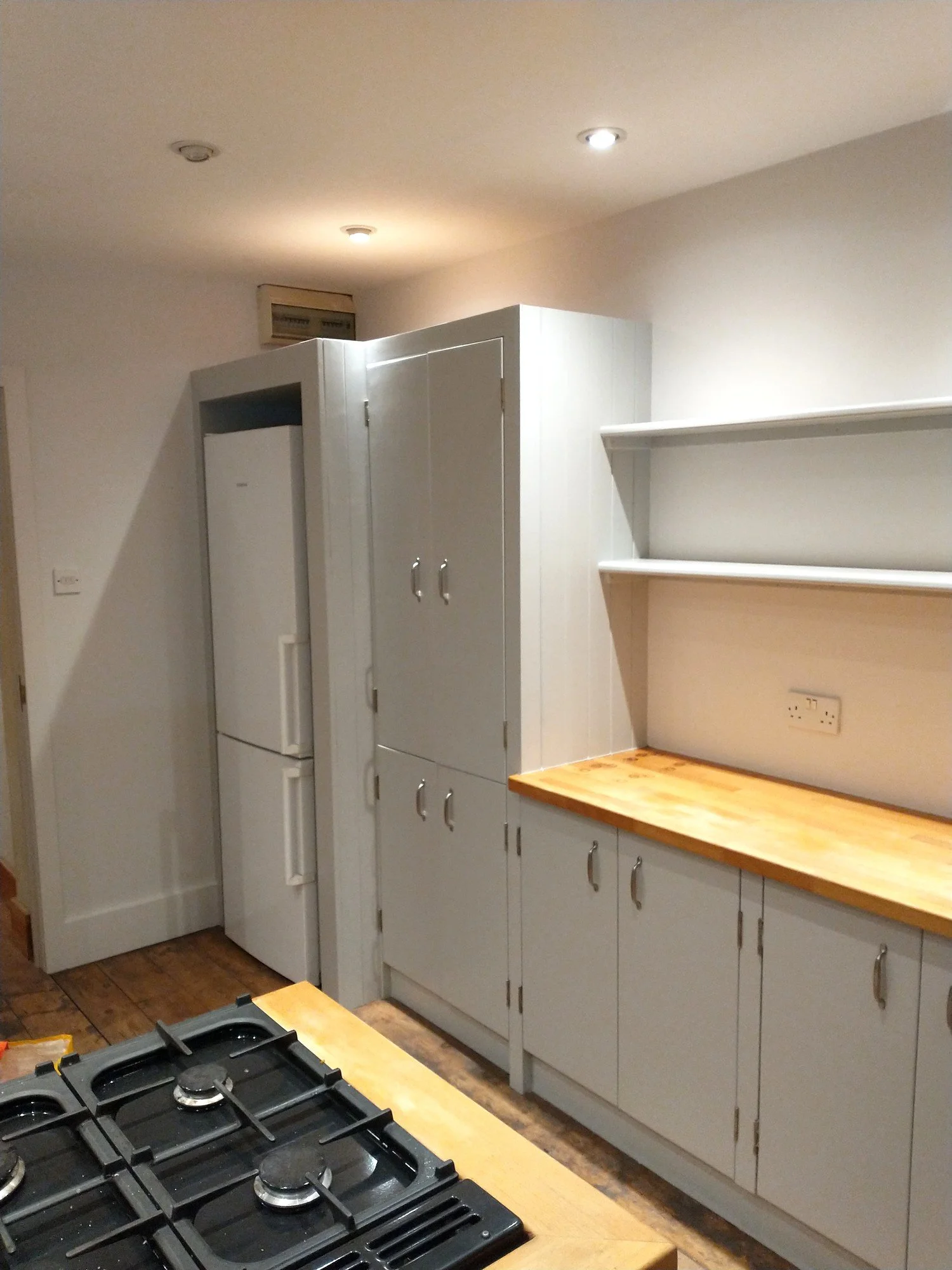 Kitchen cabinets, surrounding woodwork and wall shelves painted pale grey, with natural timber worktops retained.