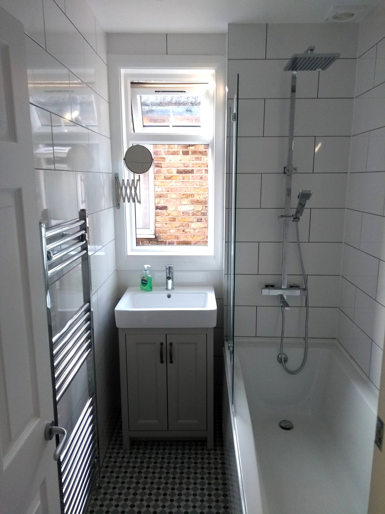 Refurbished bathroom with a grey vanity unit, glass bath screen, rainfall shower and chrome towel radiator.