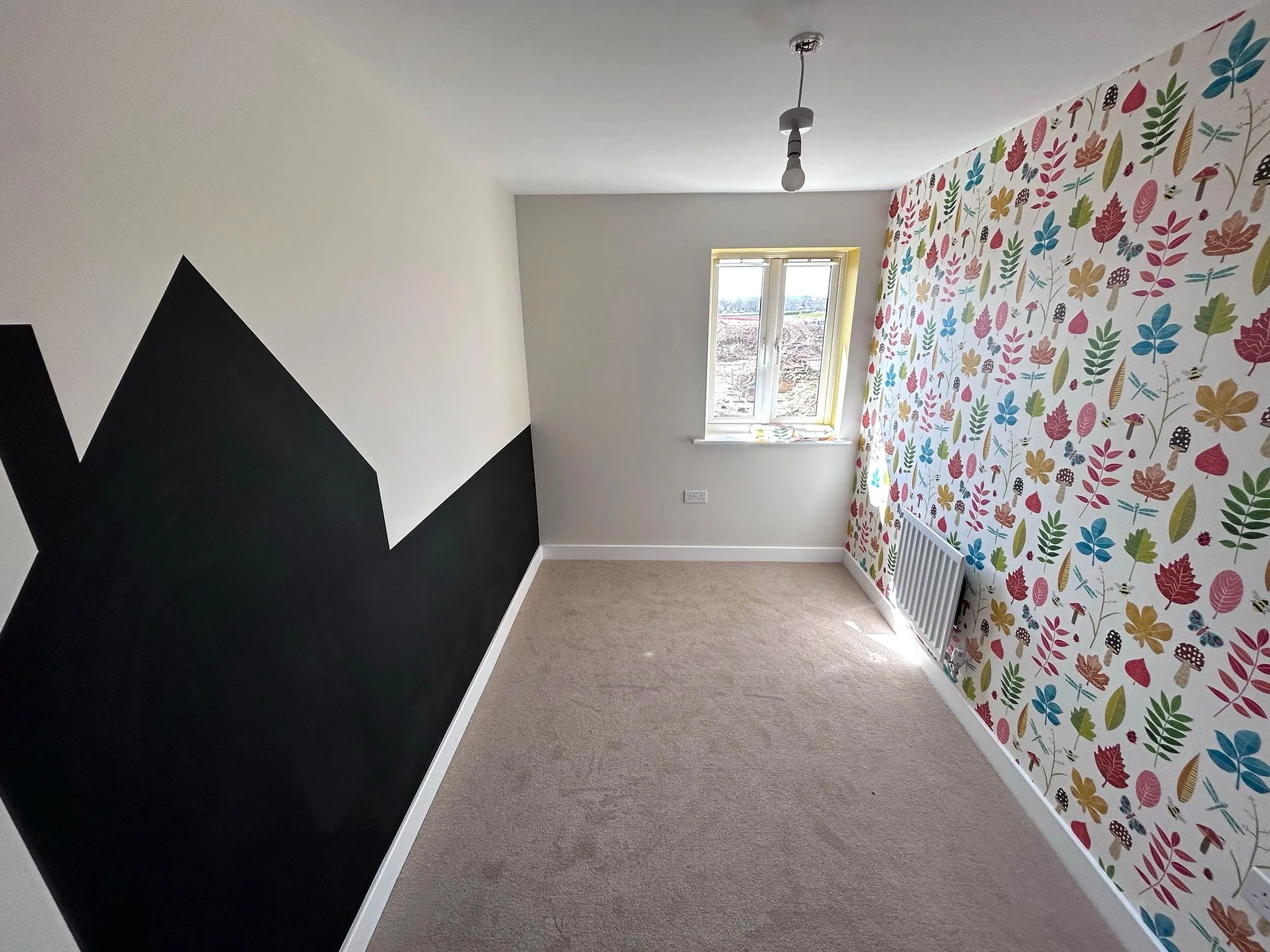 Colourful leaf-patterned feature wallpaper in a room with pale walls, white woodwork and beige carpet.