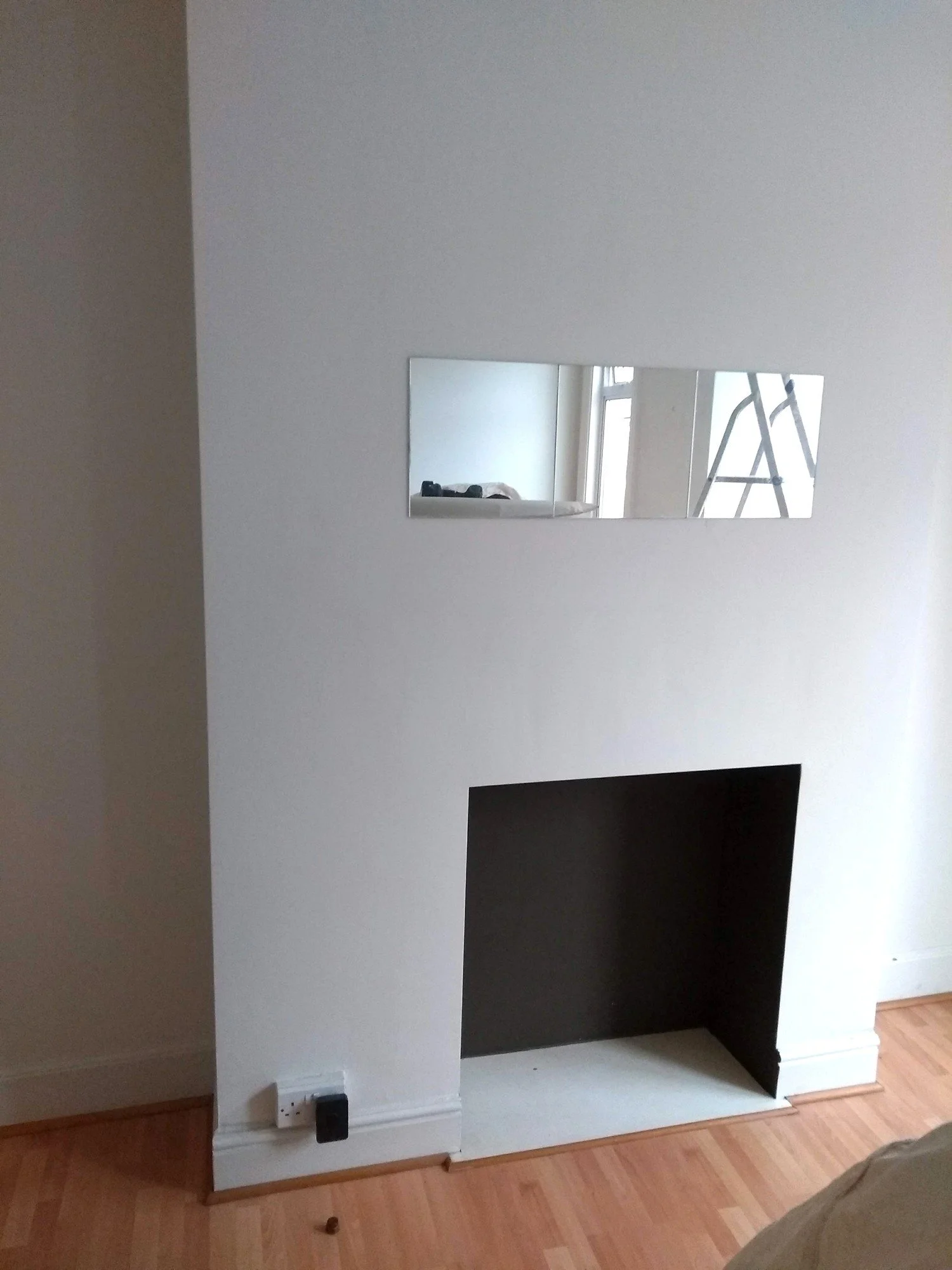 Living room chimney breast with an open fireplace recess, no surround and a rectangular mirror above.