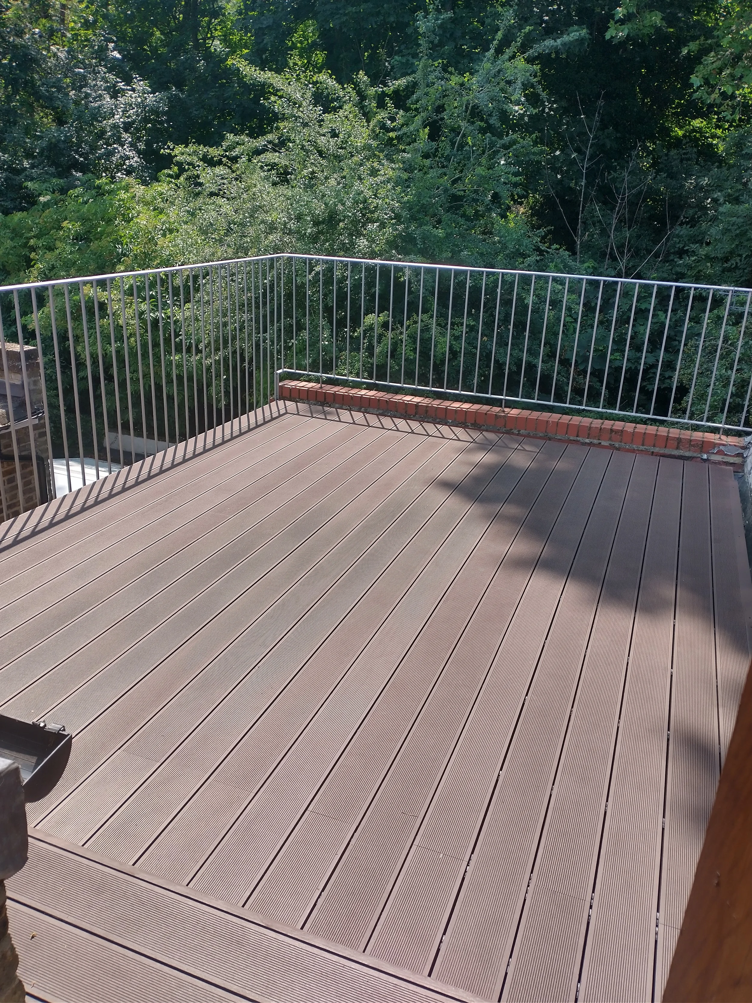 Completed brown composite decking fitted within metal terrace railings overlooking trees.