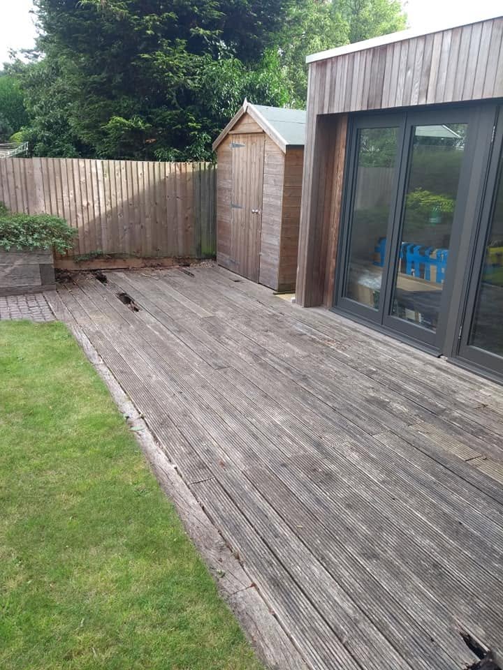 Weathered timber decking with damaged boards outside a garden room beside the lawn.