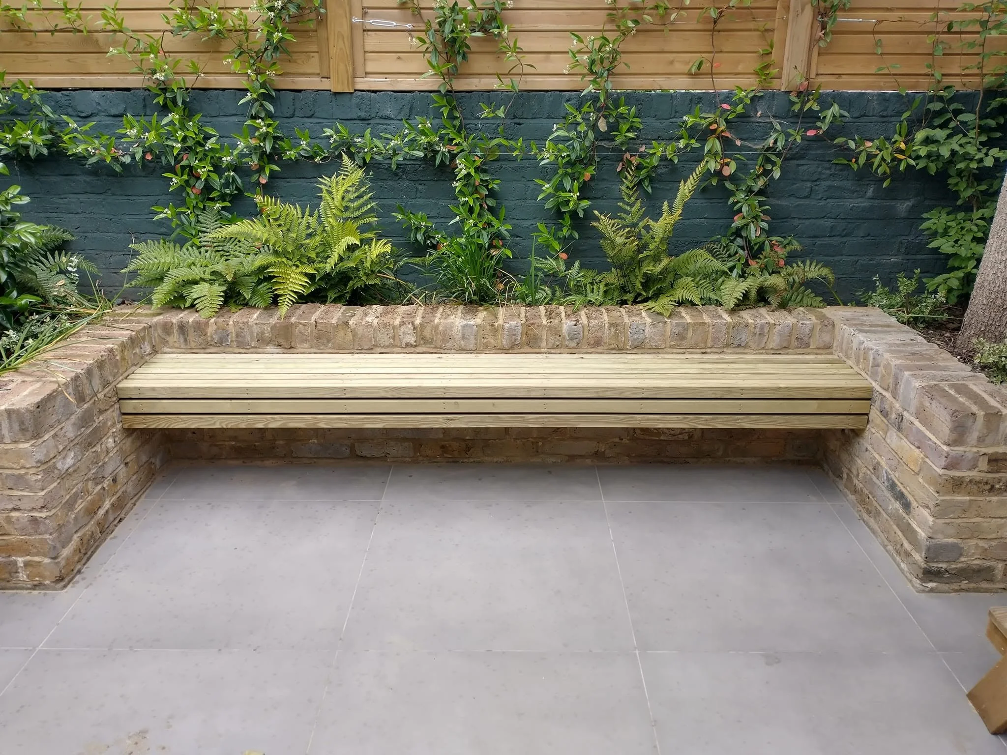 Front view of a bespoke timber bench spanning two brick raised beds, with planting behind.